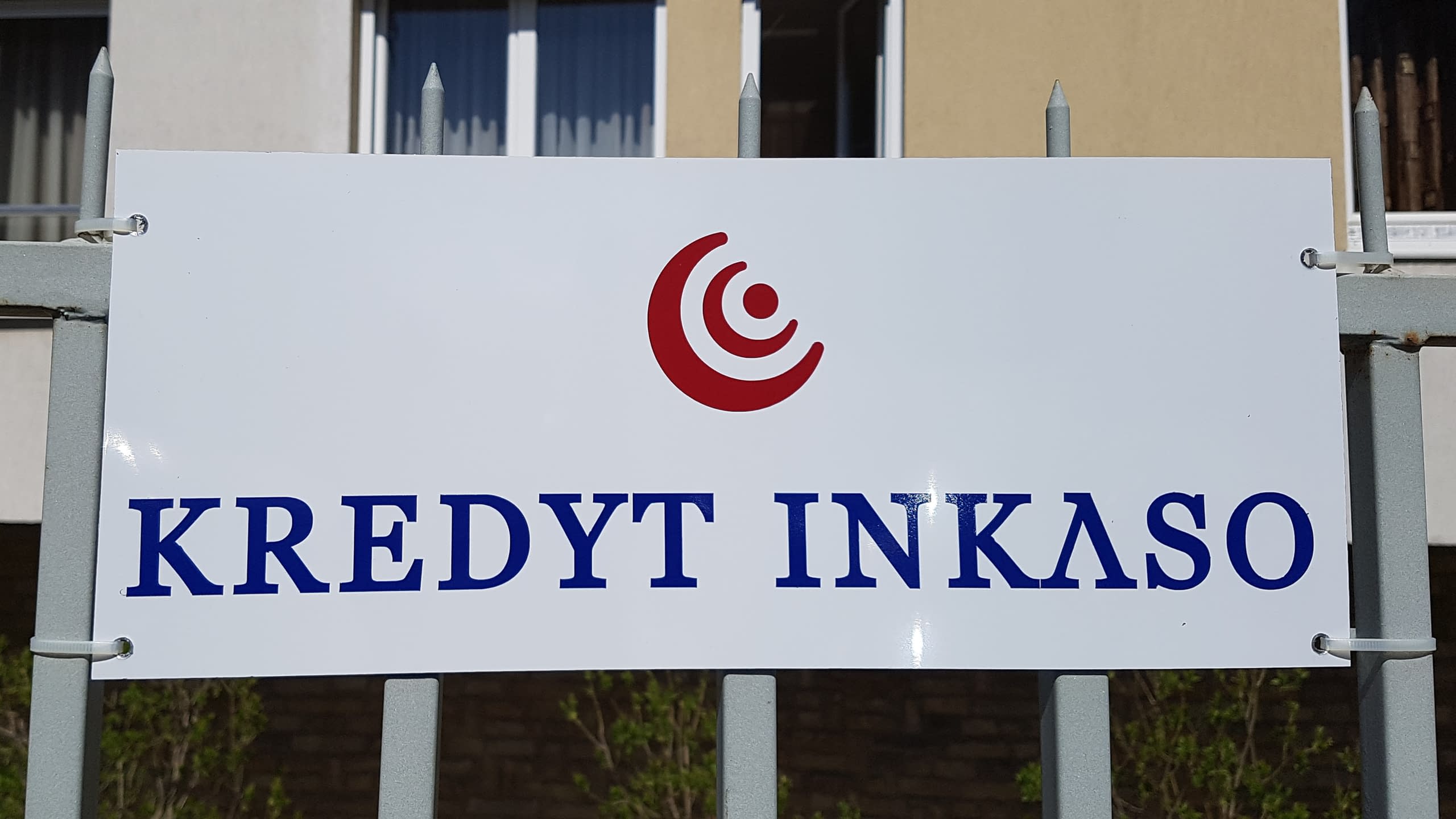 Външна фирмена табела от PVC плоскост за "KREDYT INKASO" с лого, монтирана на метална ограда.