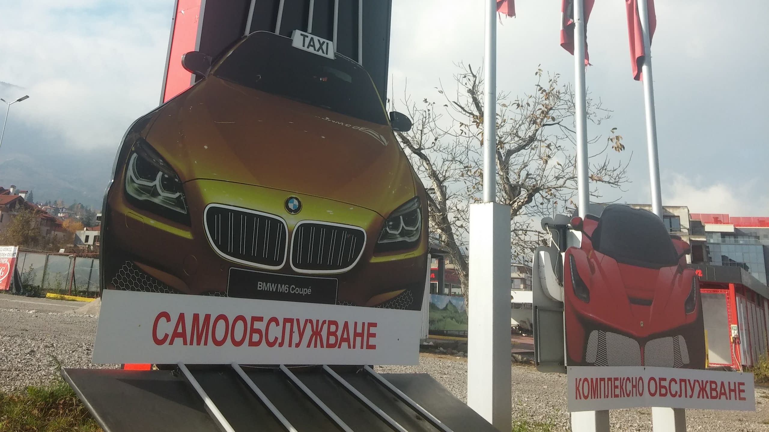 Външни фирмени табели за автомивка във формата на автомобили, указващи зони за самообслужване и комплексно обслужване.