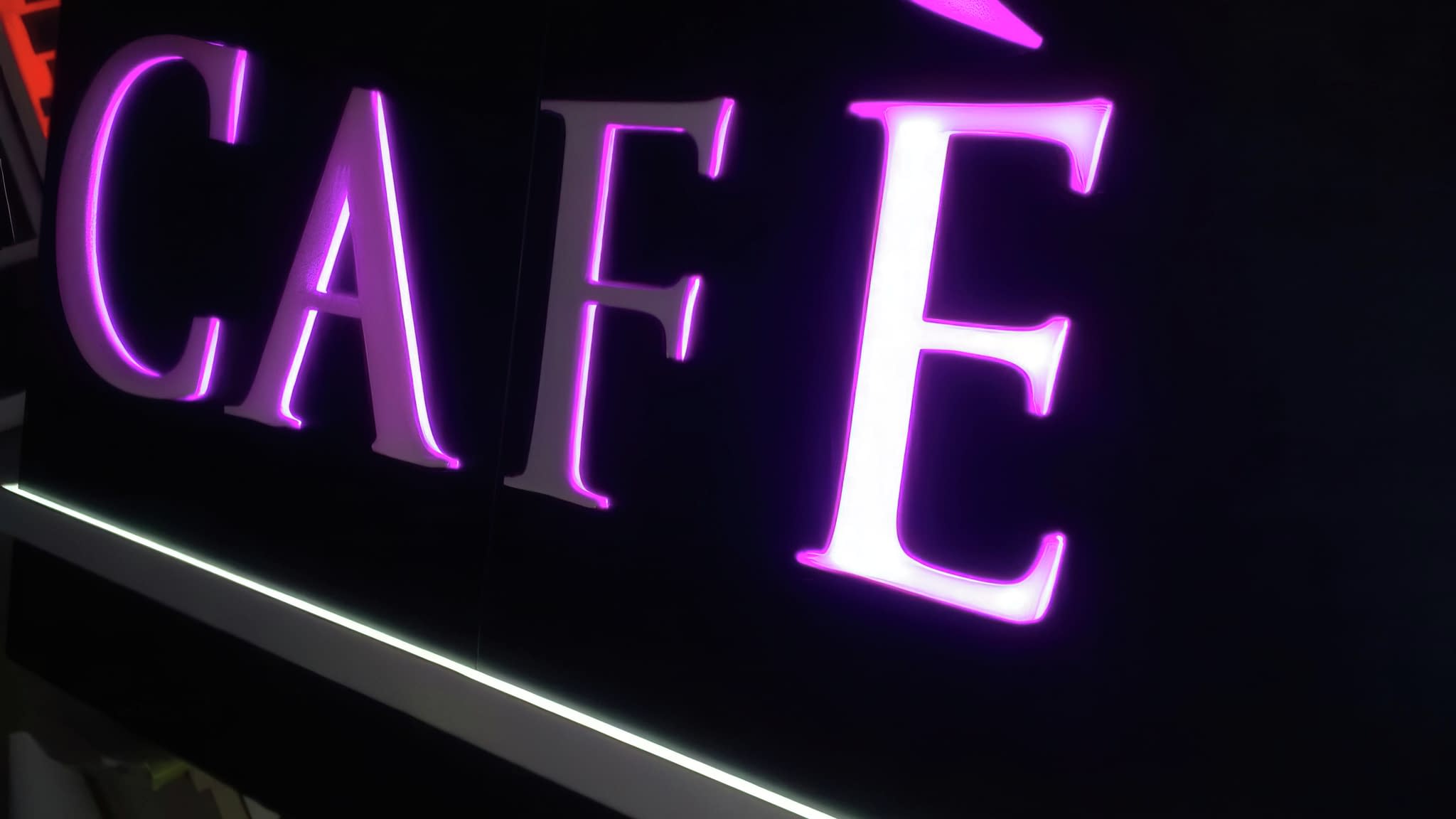 Светеща табела с надпис 'Café' с розово LED осветление на черен фон – пример за стилна реклама на заведение.