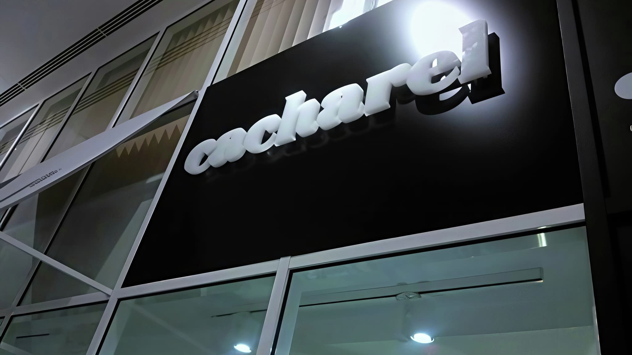 Светеща фасадна табела 'Cacharel' с бели обемни букви на черен фон – пример за стилна брандова реклама.