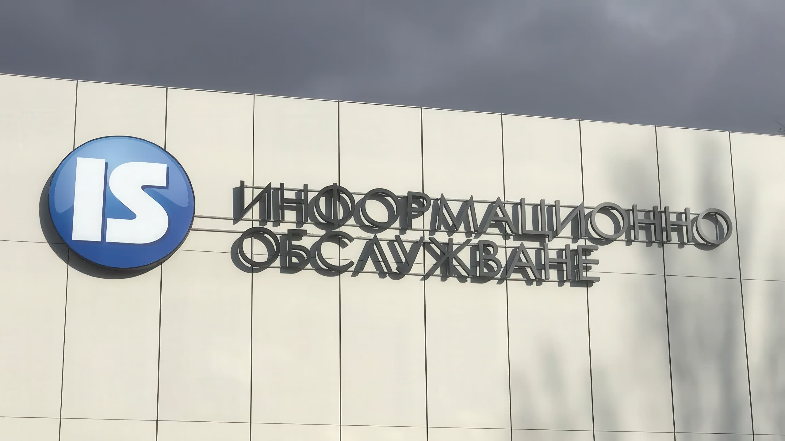 Фирмена табела на "Информационно обслужване" АД, изпълнена с несветещи обемни букви и лого върху фасада.