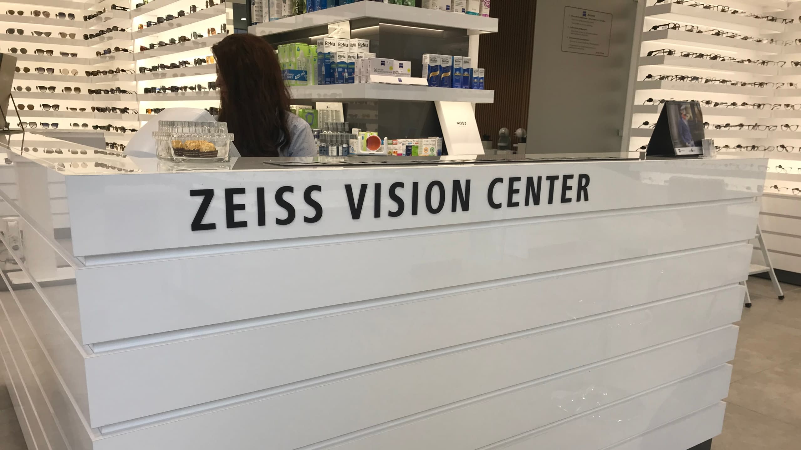 Интериорни несветещи букви от черен плексиглас с надпис "ZEISS VISION CENTER", монтирани на бяла рецепция в оптика.