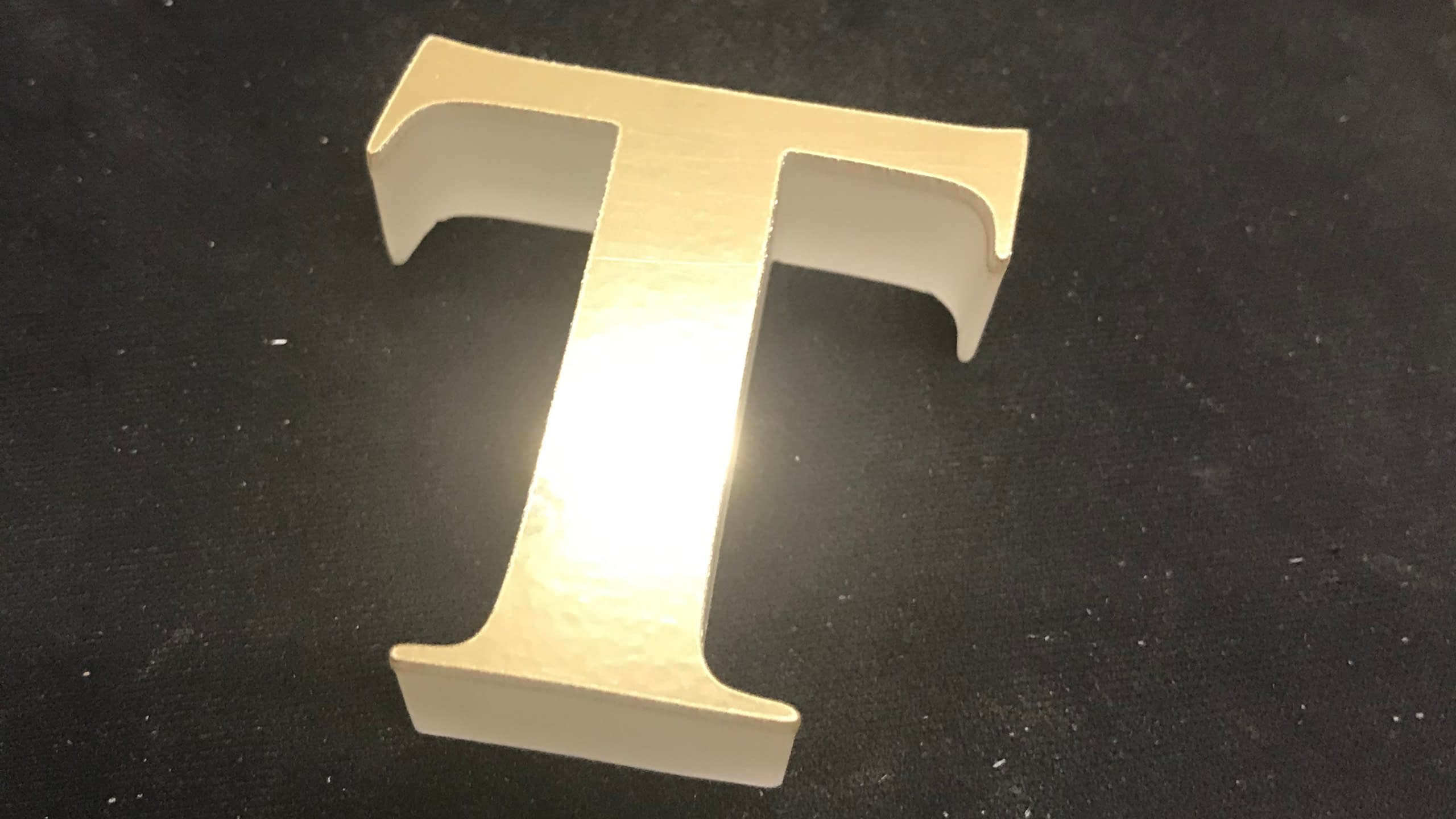 Малка декоративна обемна буква "Т" в цвят шампанско, предназначена за интериорна украса.