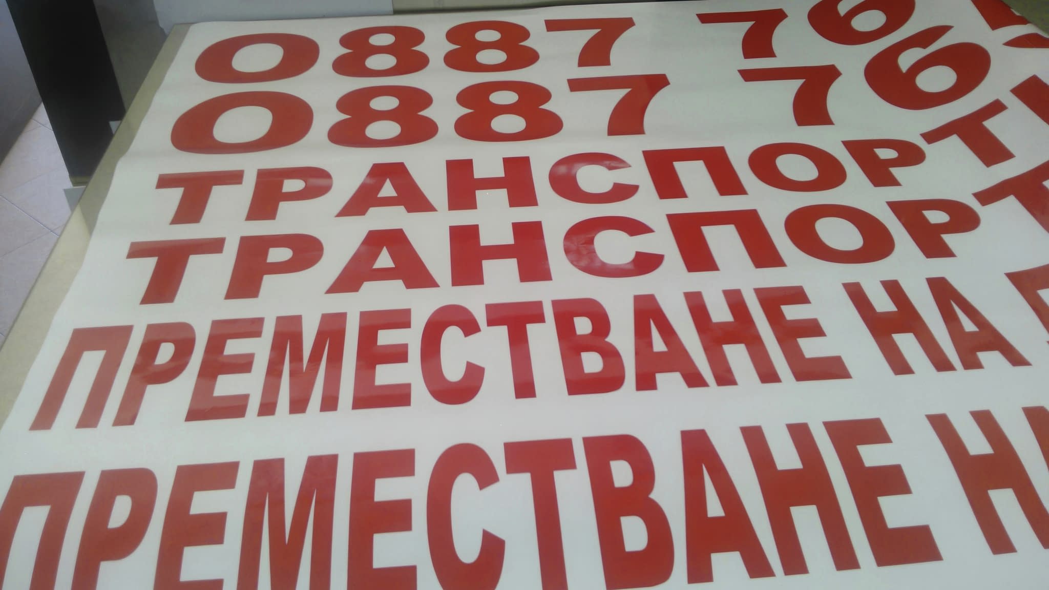 Плотерно изрязване на фолио с червен надпис за транспортни услуги и телефонен номер.