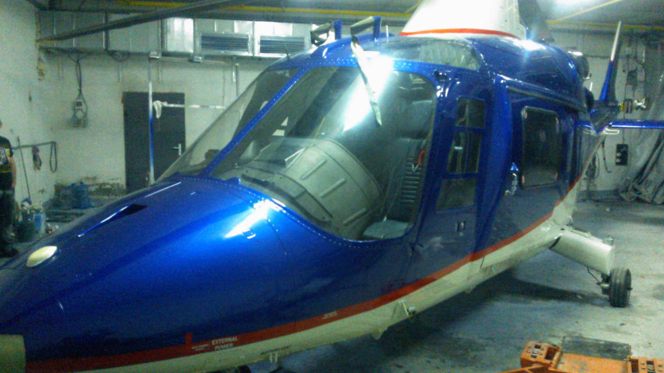 Предница на син и бял хеликоптер с червена ивица, заснет в хангар.