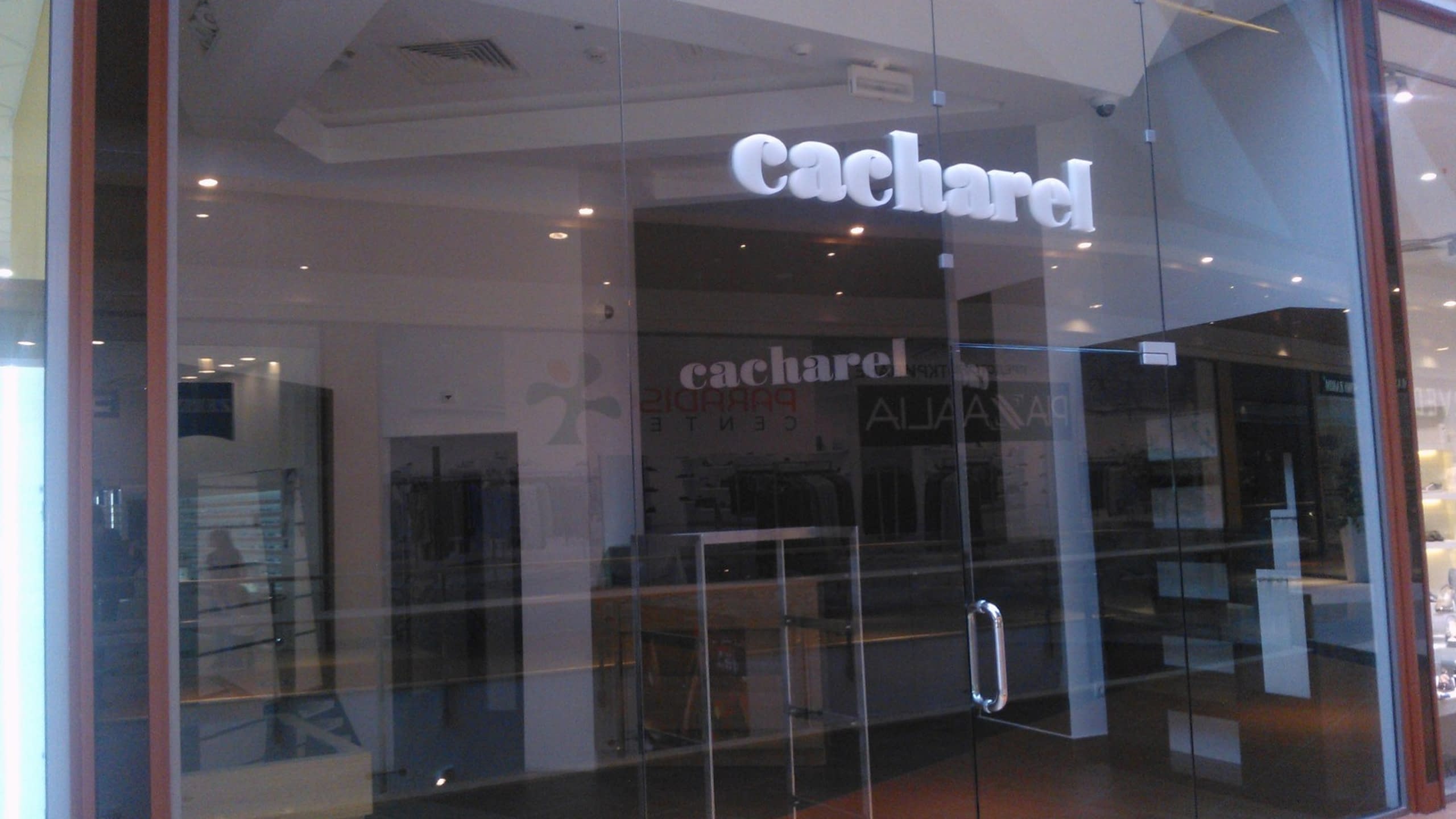 Надпис „cacharel“ с бели обемни букви, монтиран директно върху стъклената витрина на магазин.
