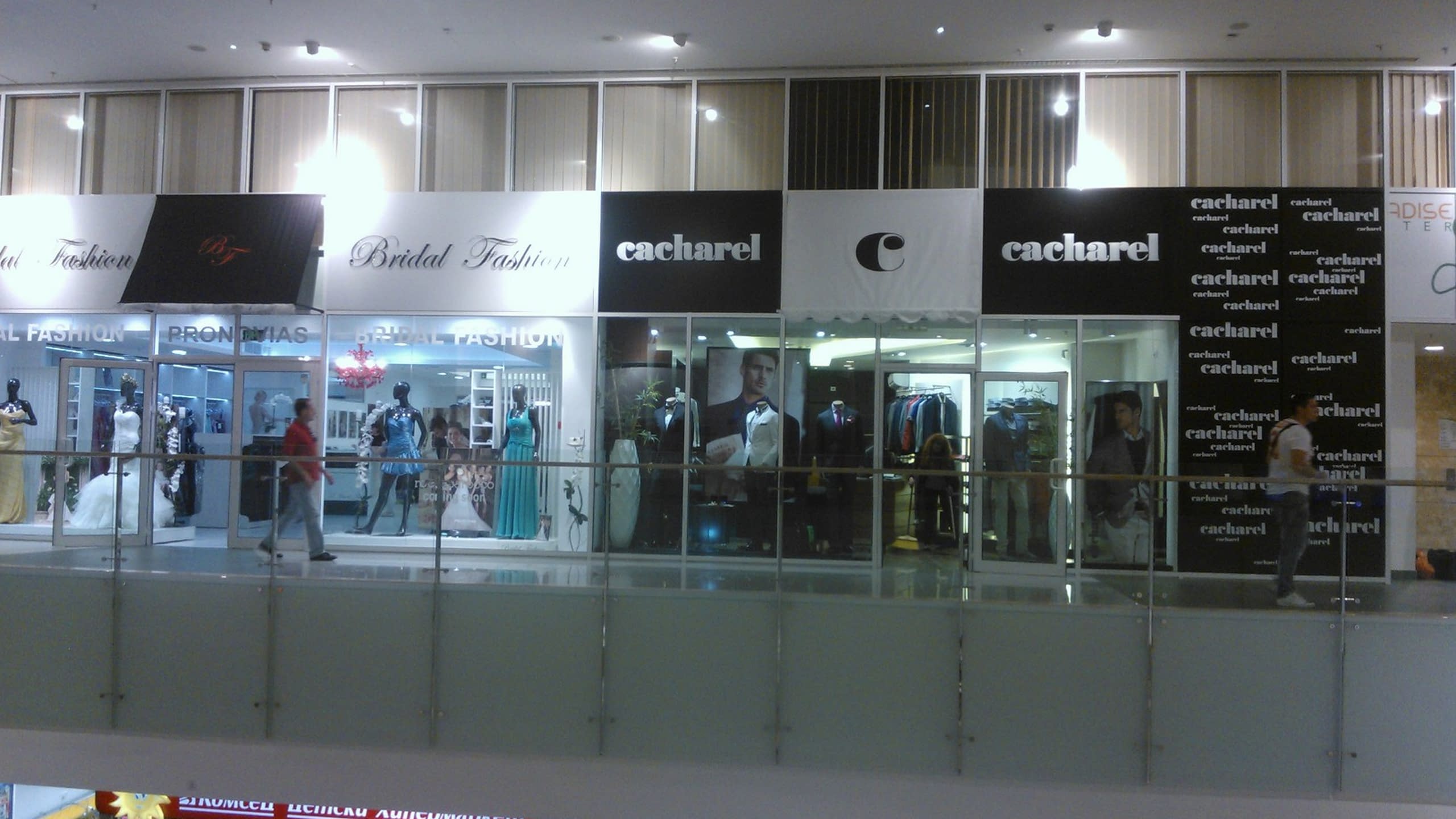 Външен изглед на съседни магазини, „Bridal Fashion“ и „Cacharel“, с големи табели с имената им над стъклените витрини.