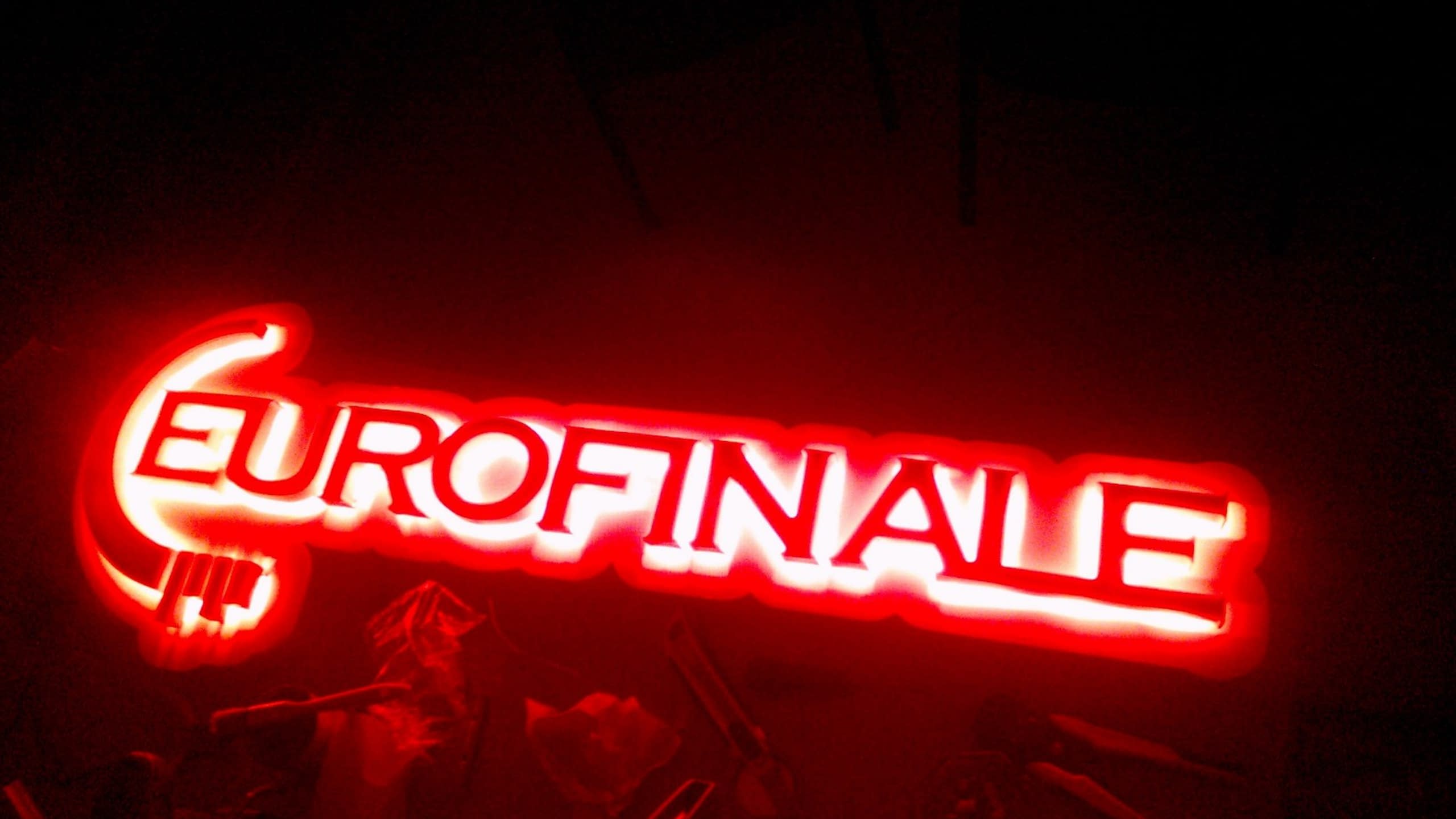 Надпис „EUROFINALE“, осветен в яркочервено в тъмно помещение.