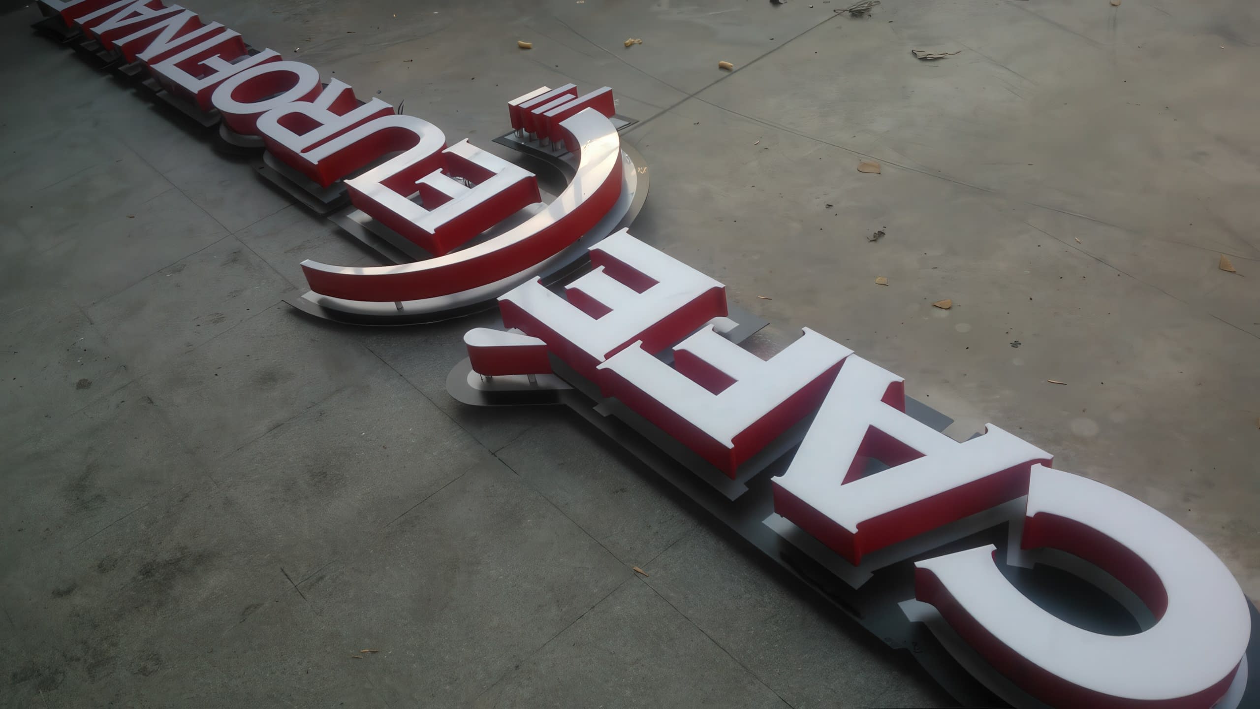 Два надписа с обемни букви с бяло лице и червени страници, разположени на бетонен под.