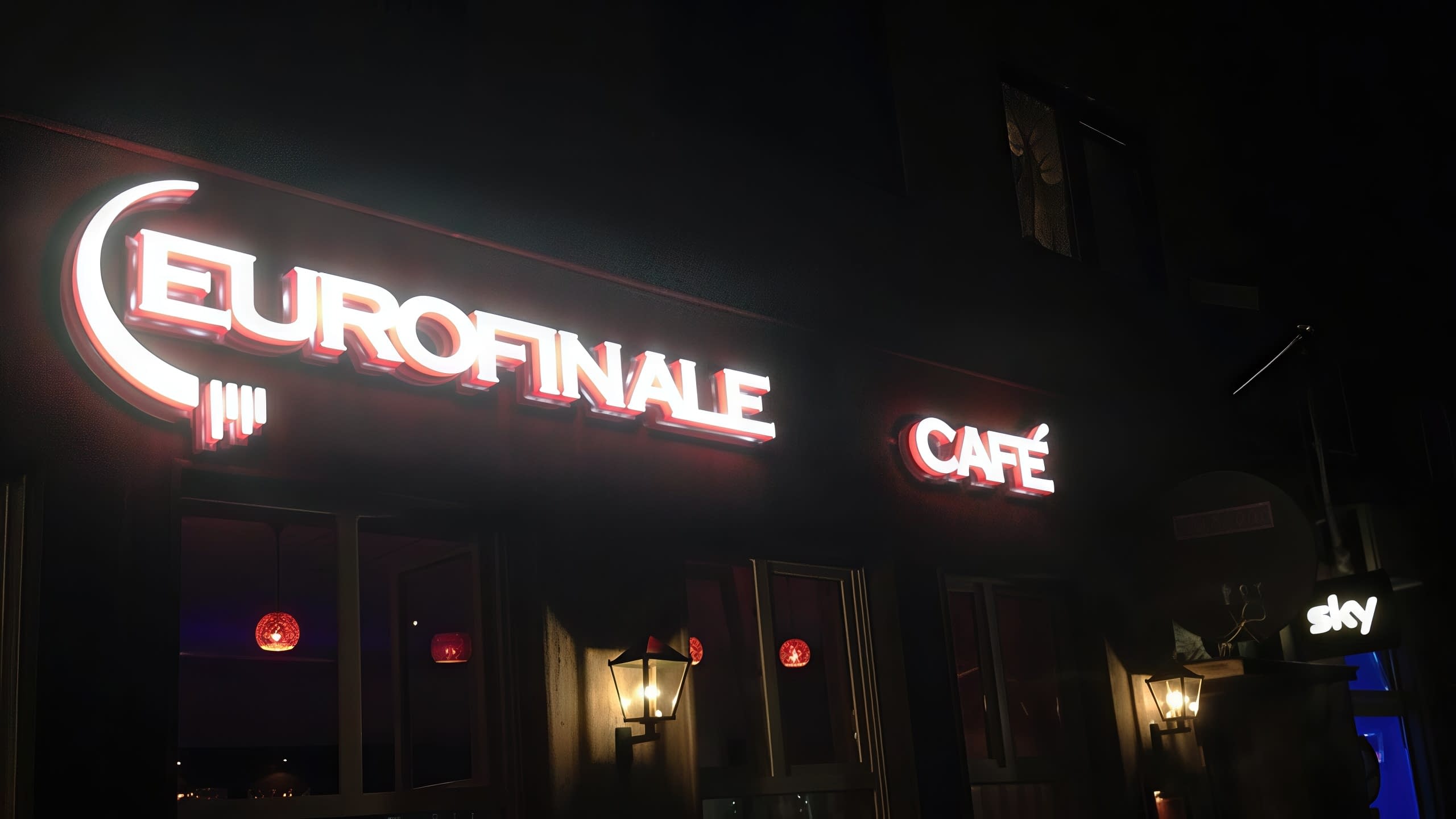 Нощна снимка на фасада на заведение с два светещи надписа – „Eurofinale“ и „Café“.