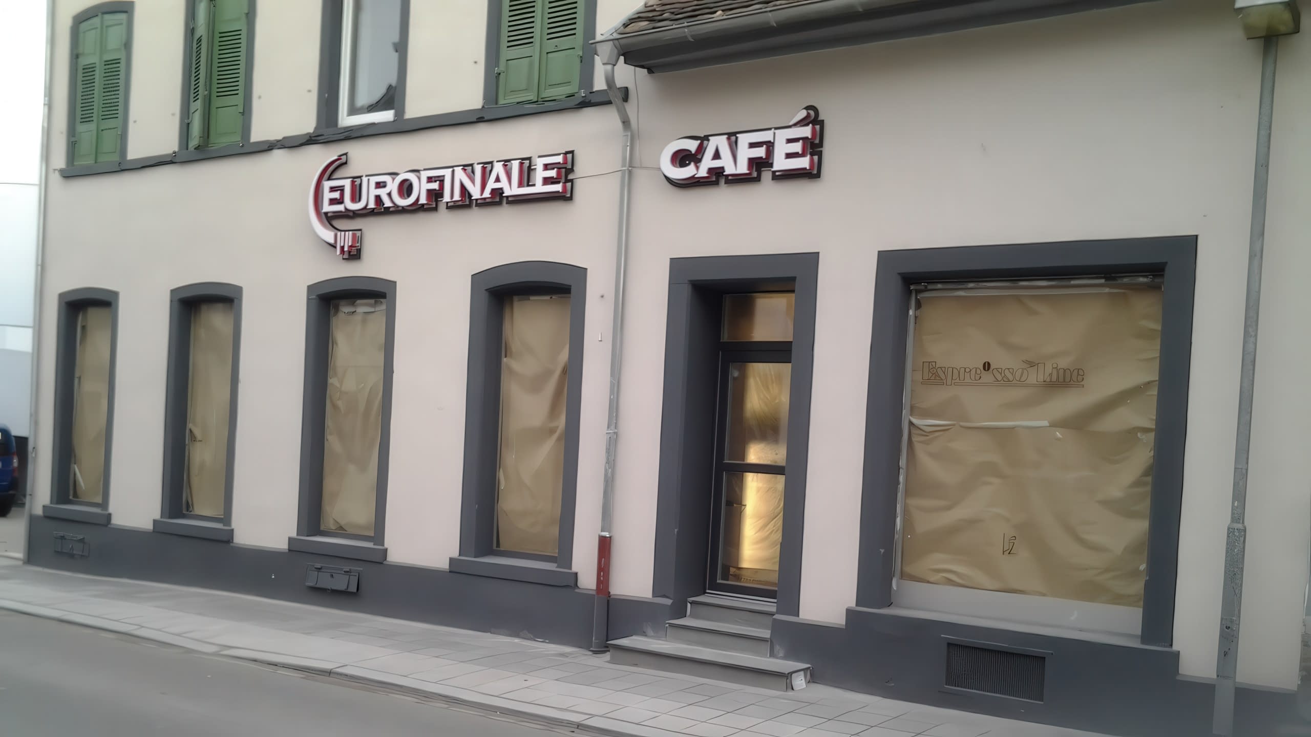 Дневна снимка на фасада на сграда с монтирани надписи „Eurofinale“ и „Café“ и прозорци, покрити с хартия.