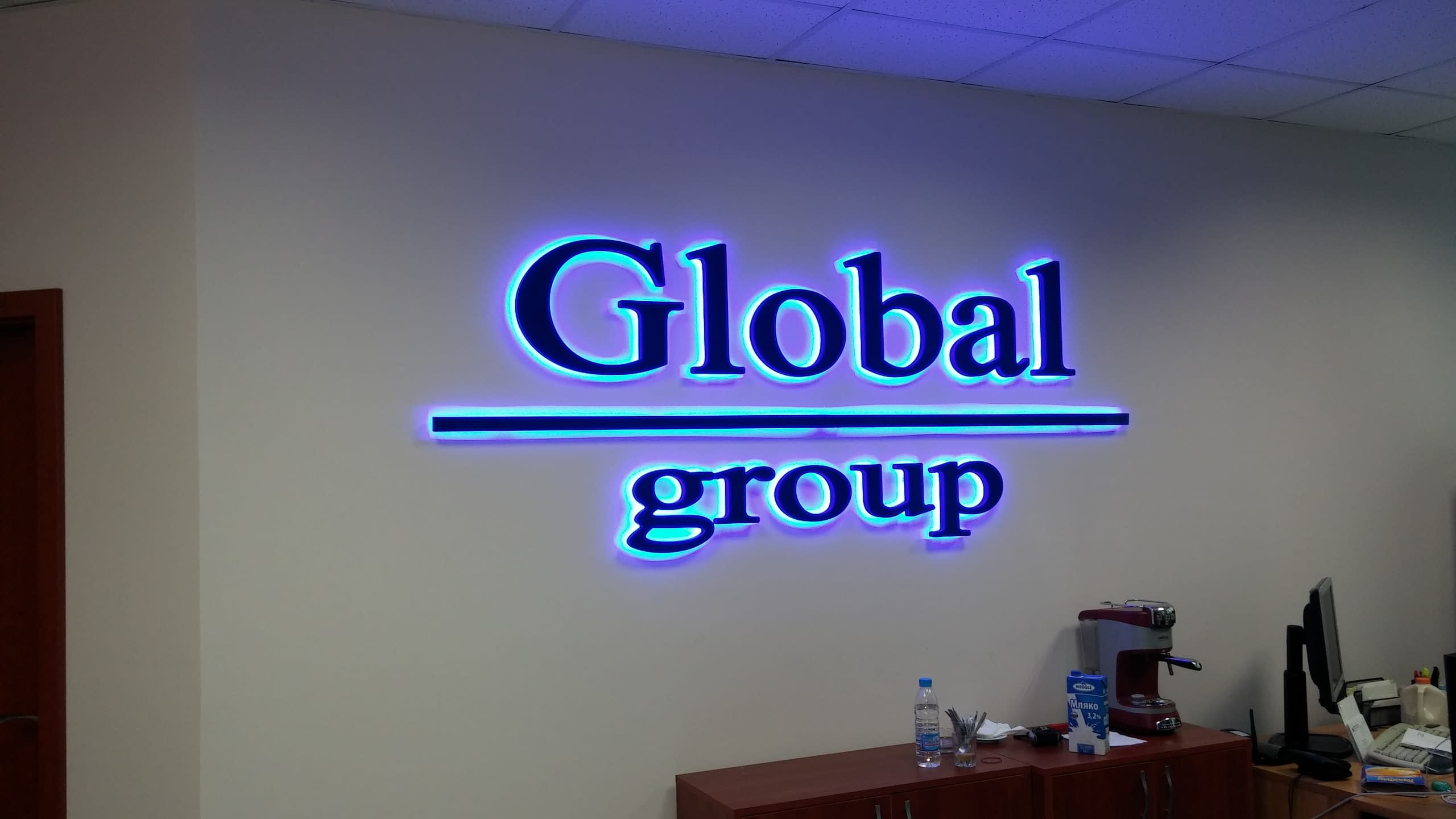 Надпис „Global group“ на стена в офис, осветен със синя контурна светлина.