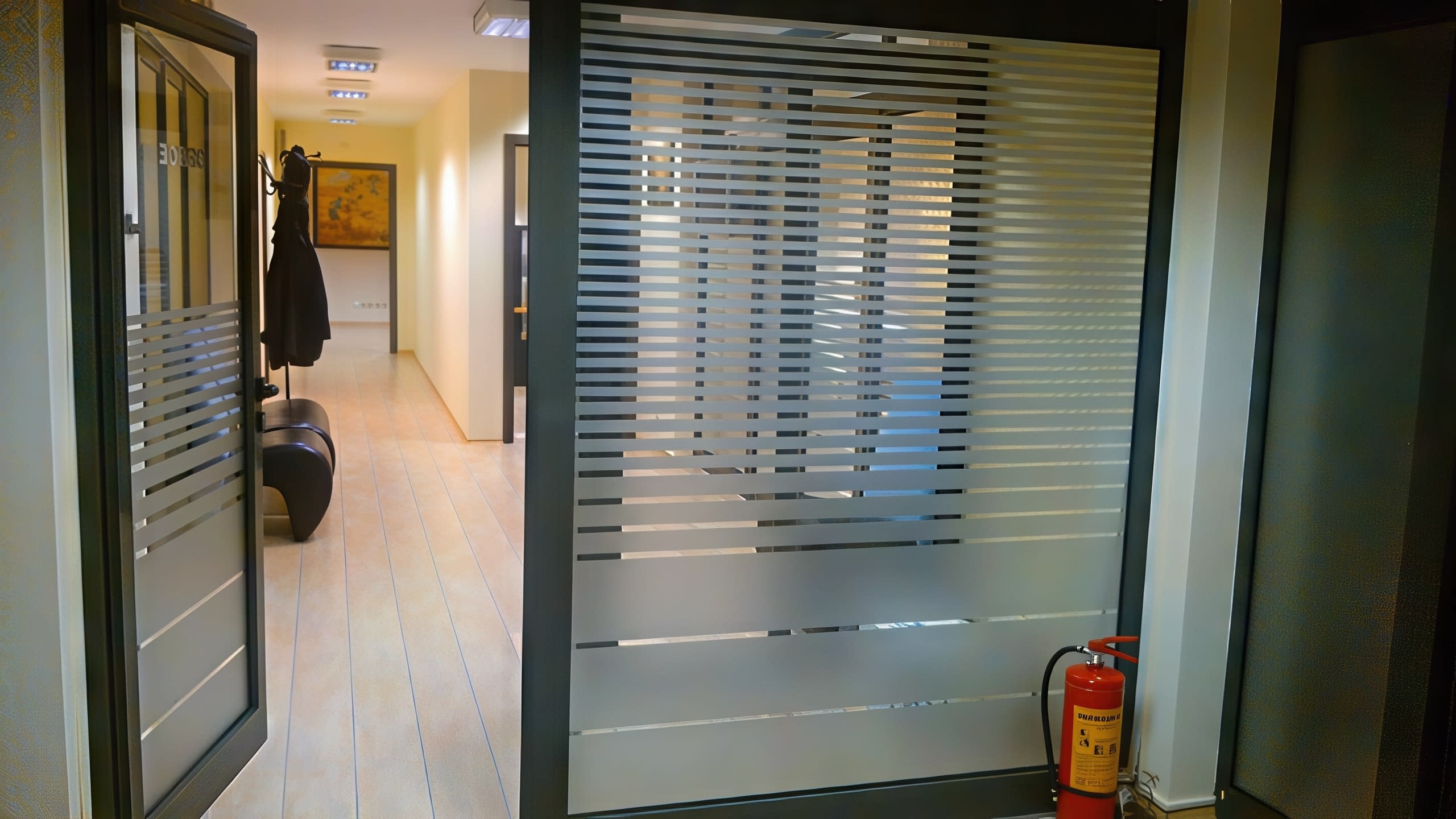 Интериор на офис коридор със стъклени стени и врати, облепени с матирано фолио на хоризонтални ивици.