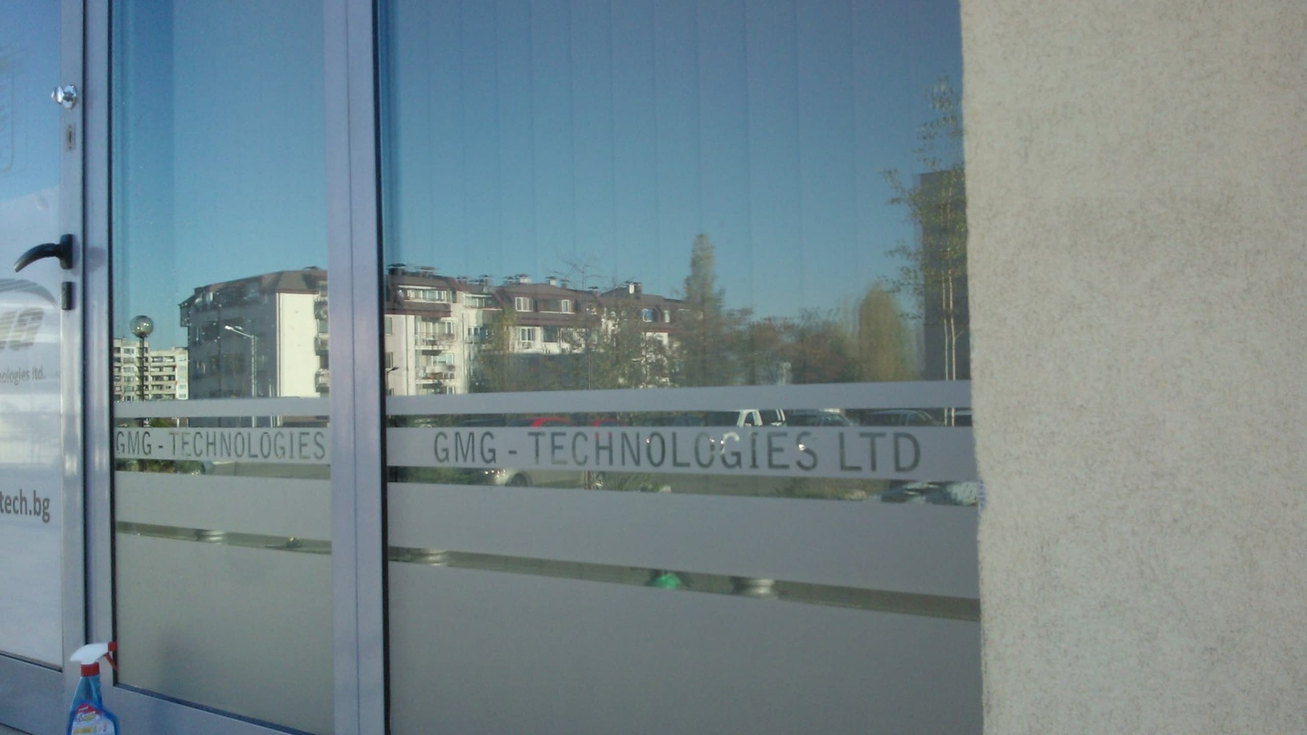Стъклен вход на офис, облепен с фолио с ефект на матирано стъкло, с изрязан надпис „GMG-TECHNOLOGIES LTD“.