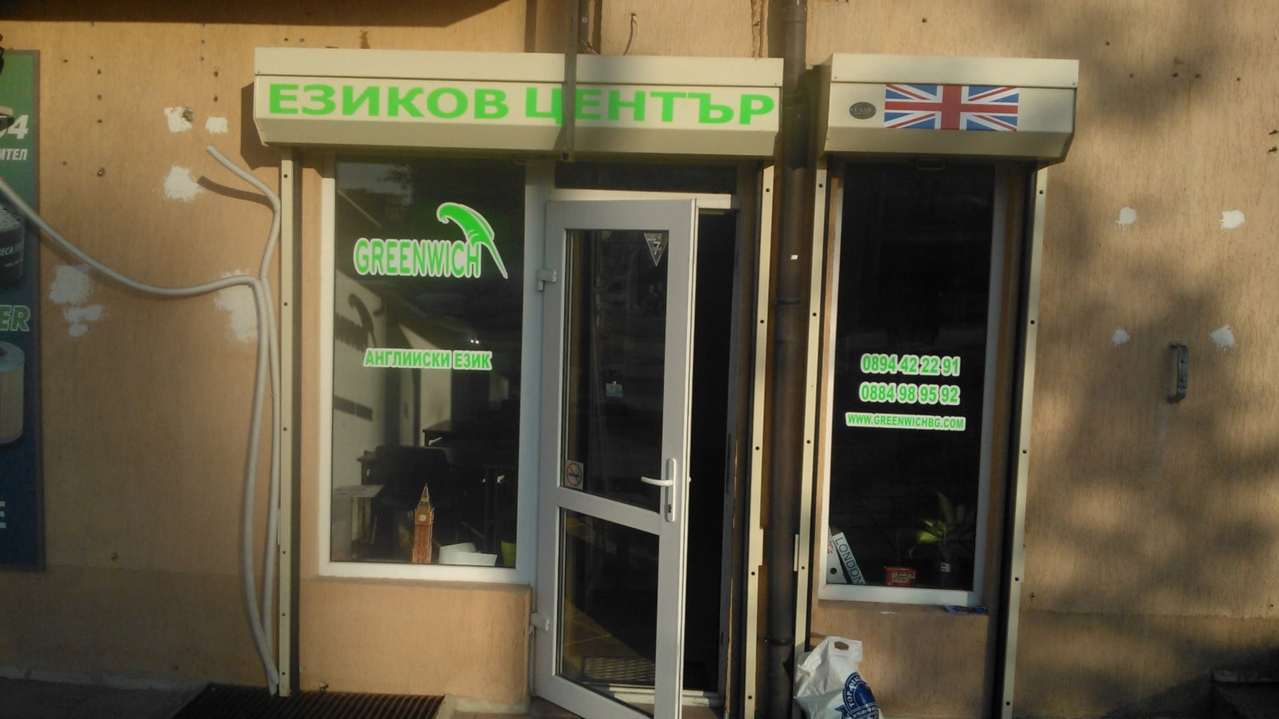 Вход на обект с надпис „Езиков център“, стикери със зелен текст по стъклата и британско знаме.