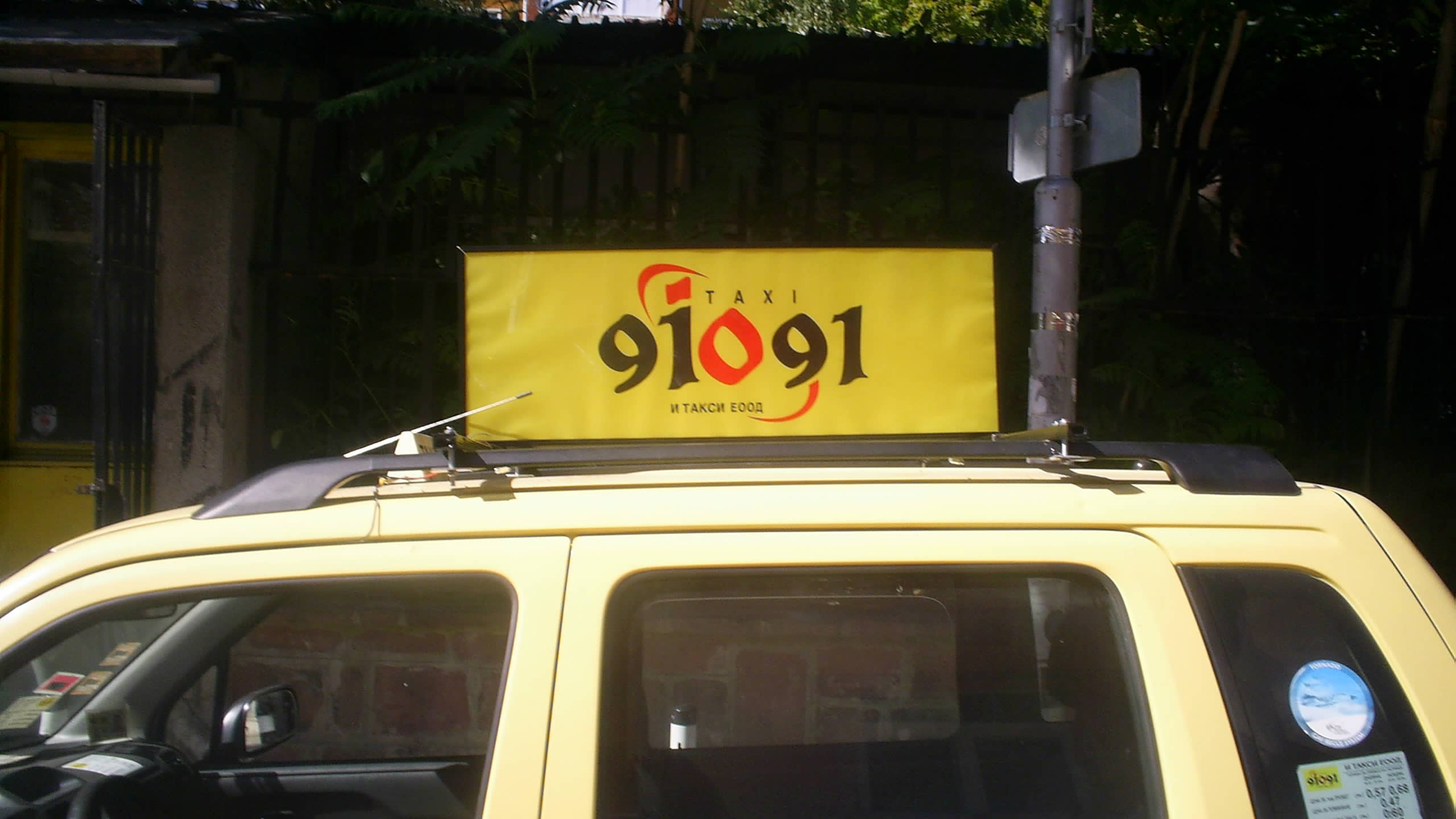 Жълта табела с номер 91091, монтирана на покрива на таксиметров автомобил.
