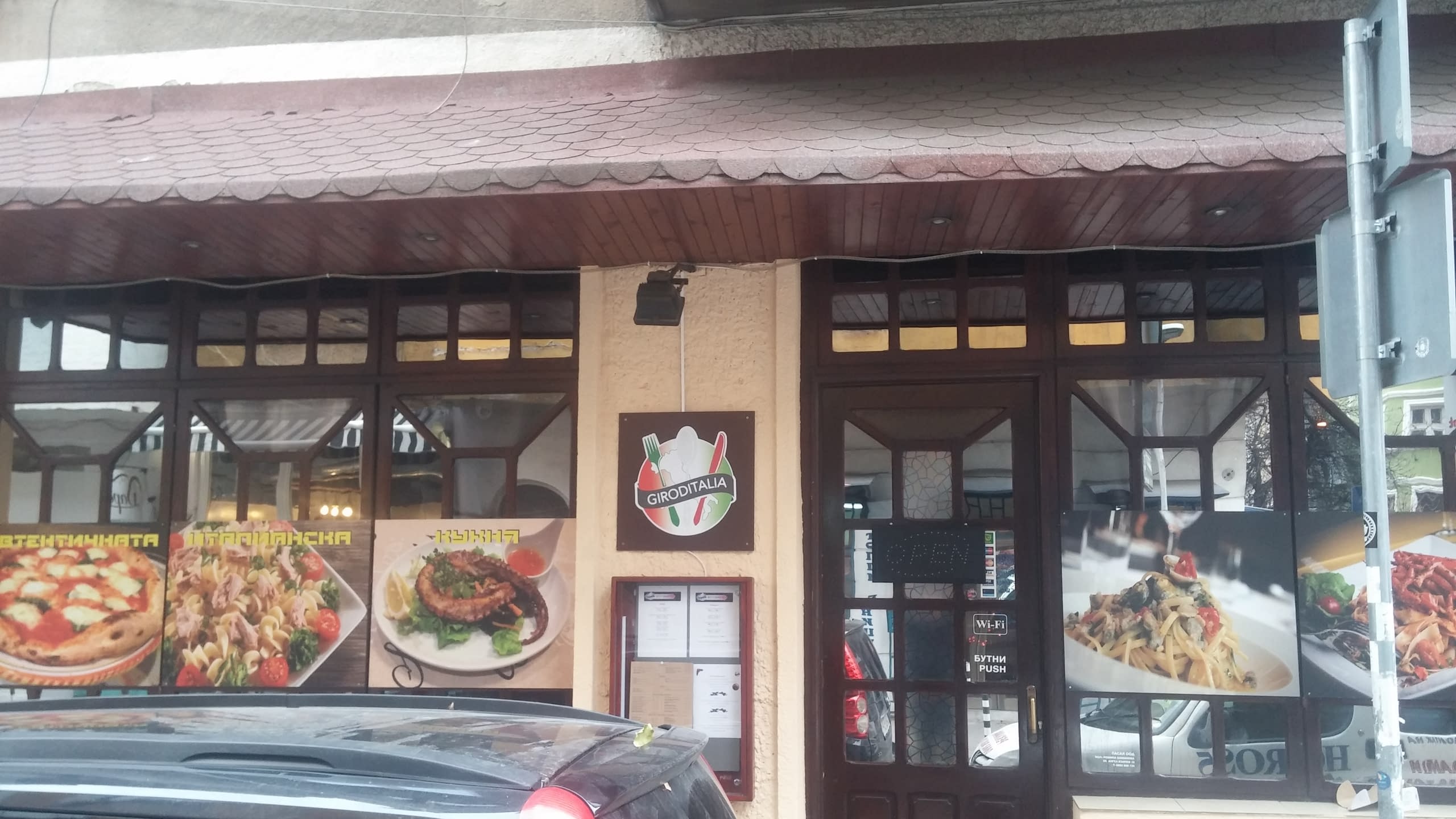 Фасада на италиански ресторант с табела с лого и големи снимки на храна по витрините.