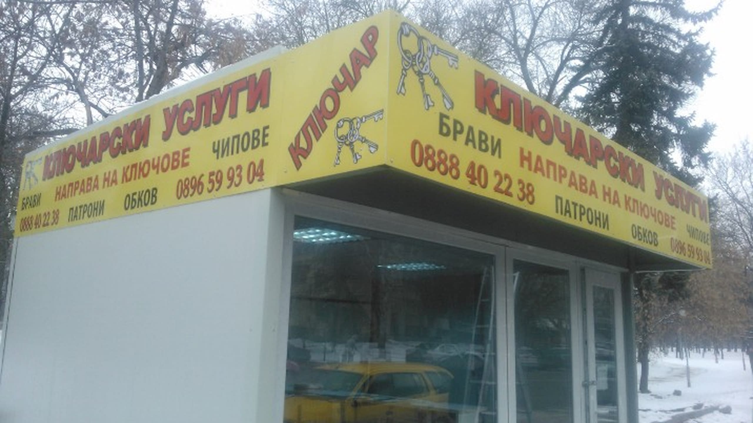 Жълта ъглова табела на павилион за ключарски услуги, на фона на зимни дървета.