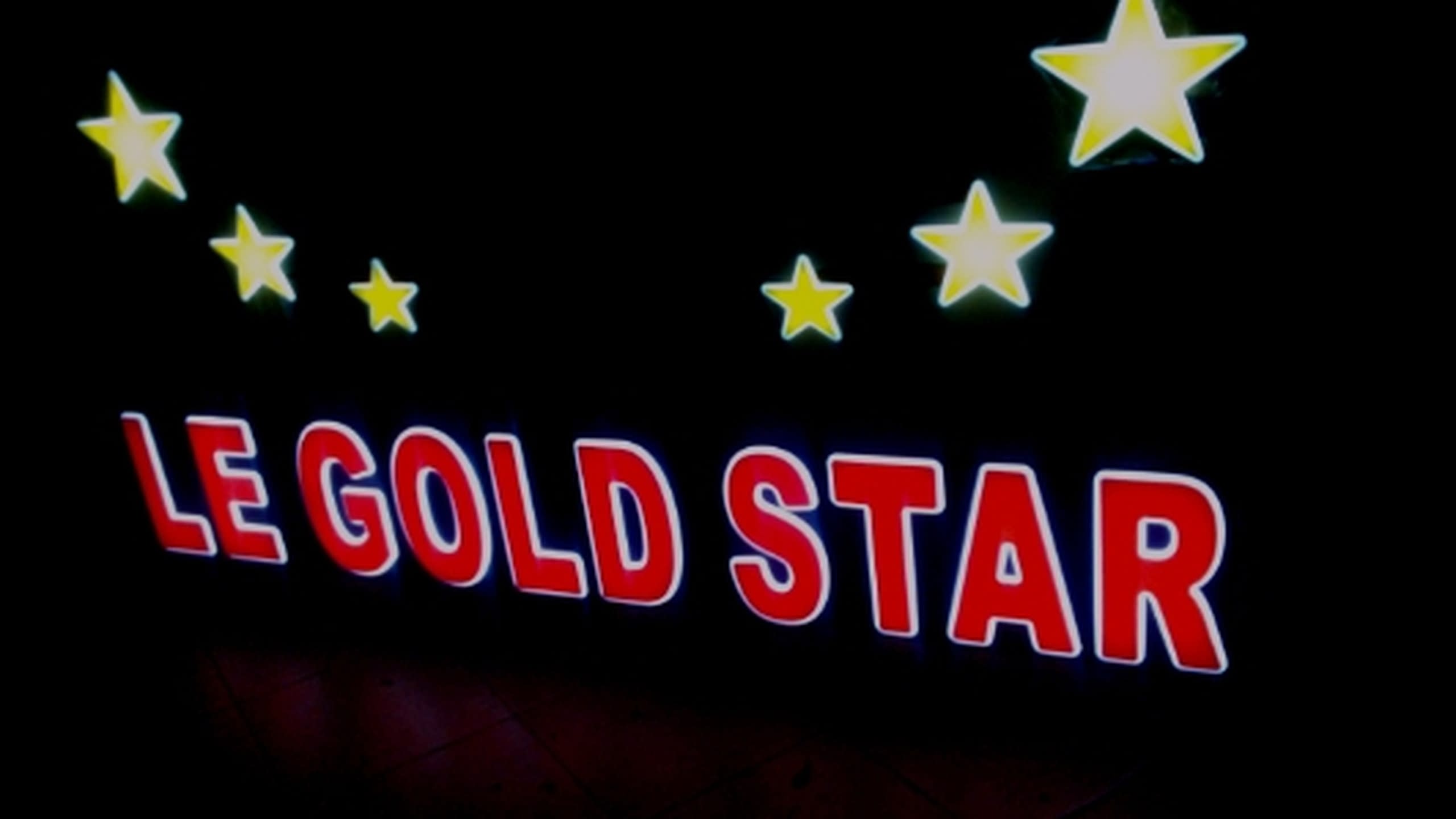 Червени букви и жълти звезди със светещ бял контур, заснети в близък план на изцяло черен фон.