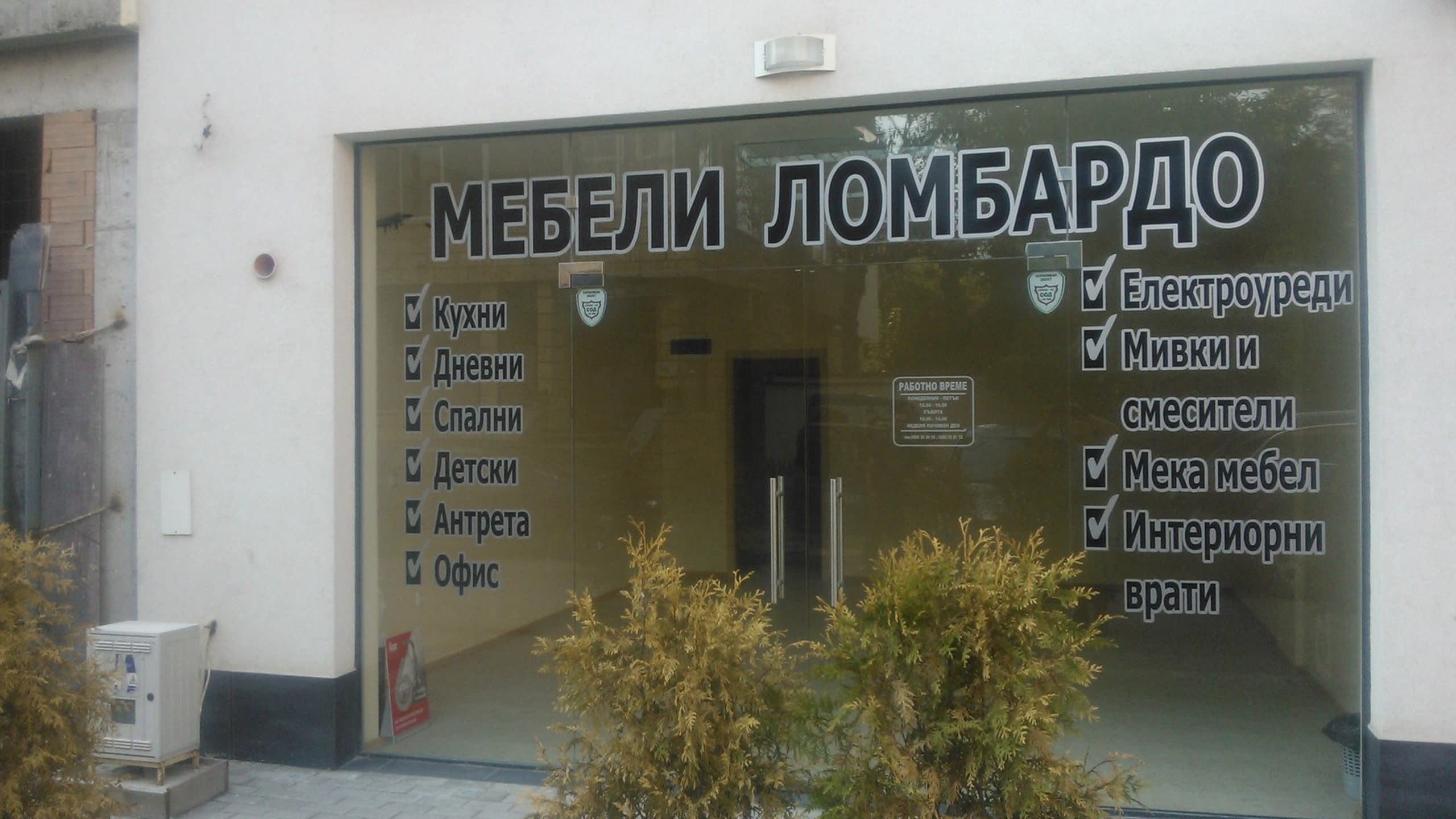 Стъклена фасада на мебелен магазин с надписи от бяло фолио, изброяващи видовете предлагани мебели.
