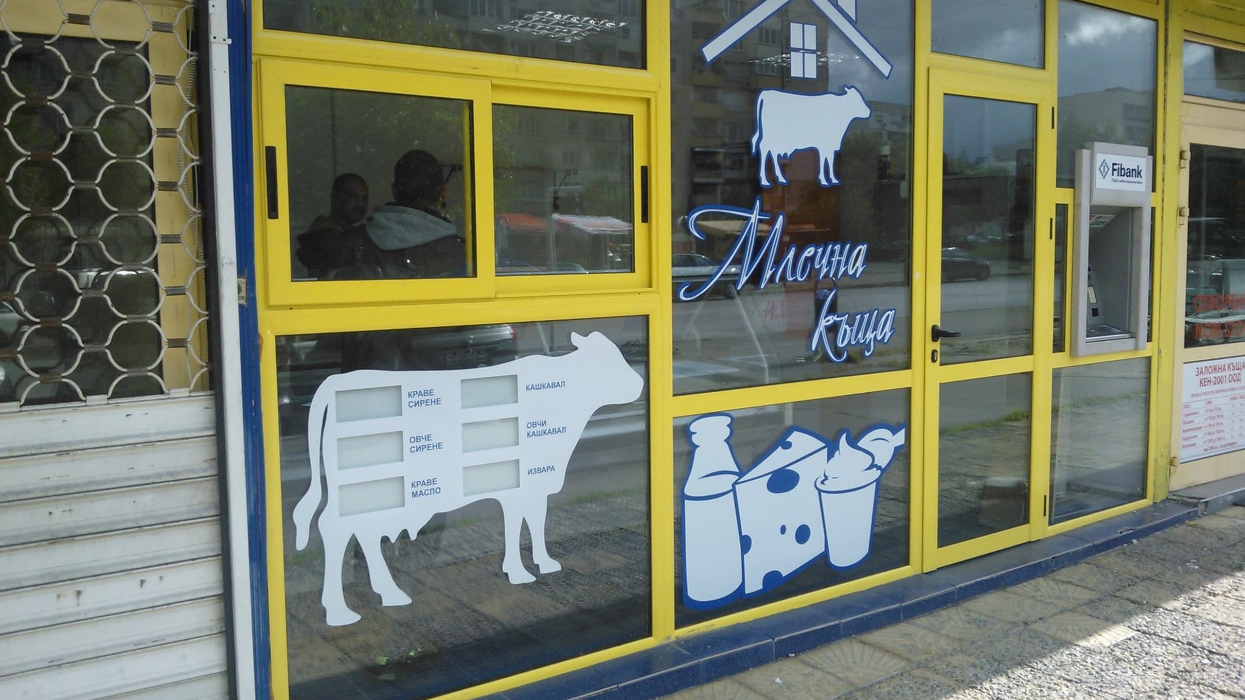 Цялостен изглед на витрина на магазин "Млечна къща", брандирана със стикери на крави и млечни продукти.