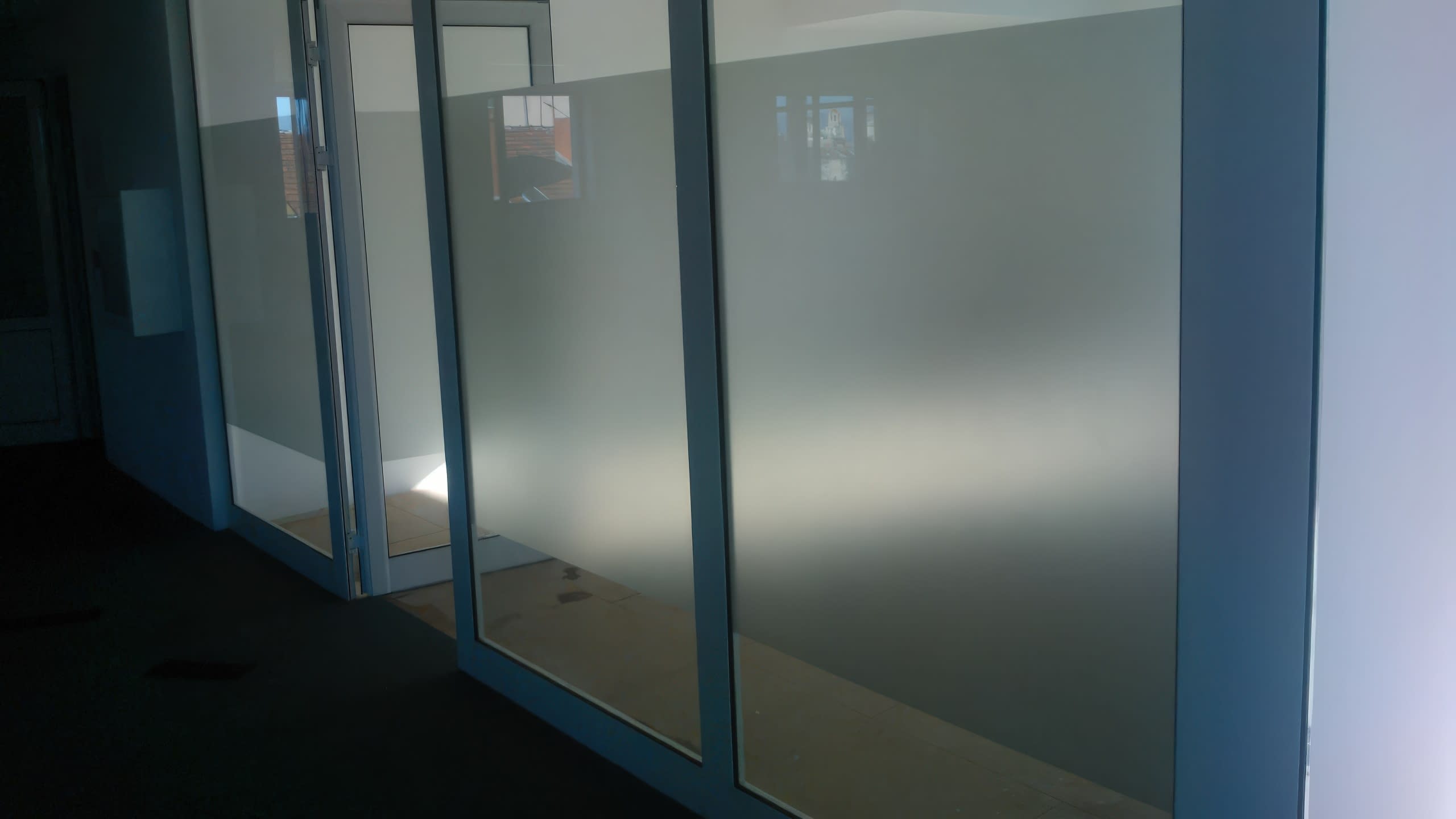 Стъклени стени на празен офис, частично облепени с хоризонтална ивица от матирано фолио.