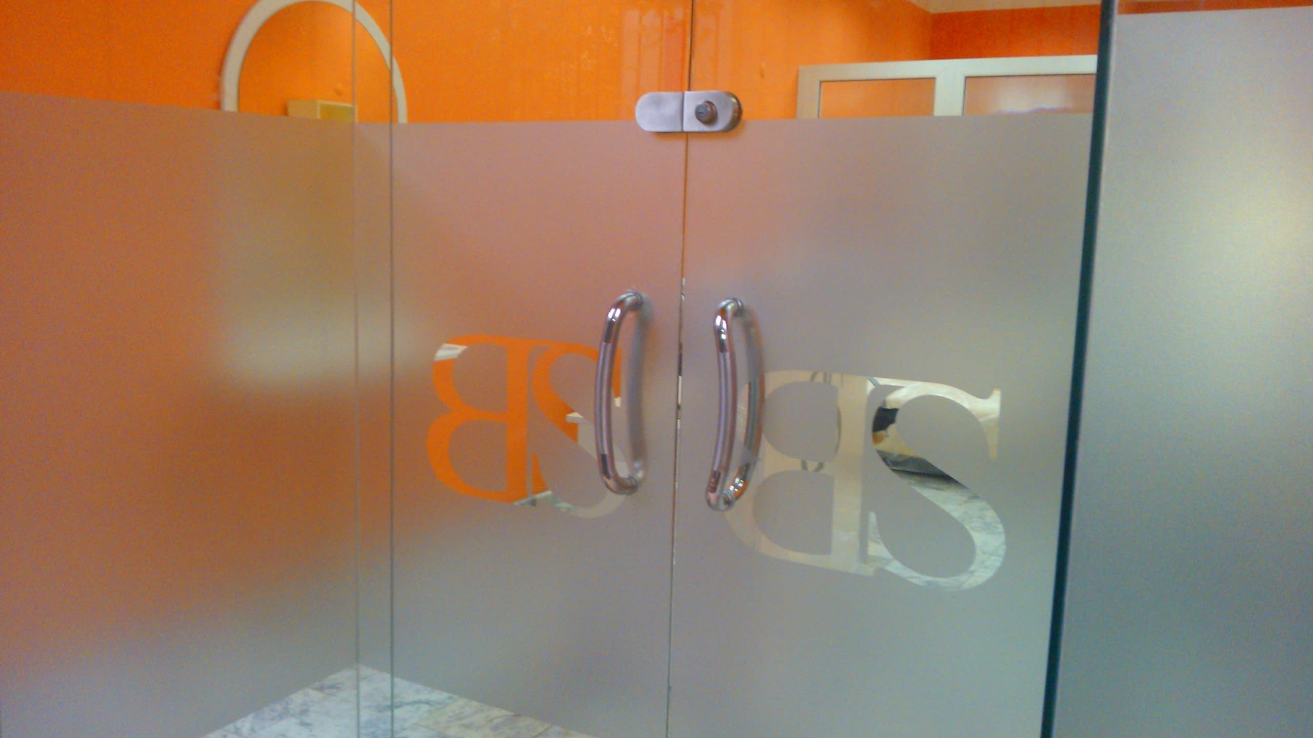 Стъклена врата, облепена с матирано фолио, с изрязано в него лого "BS".