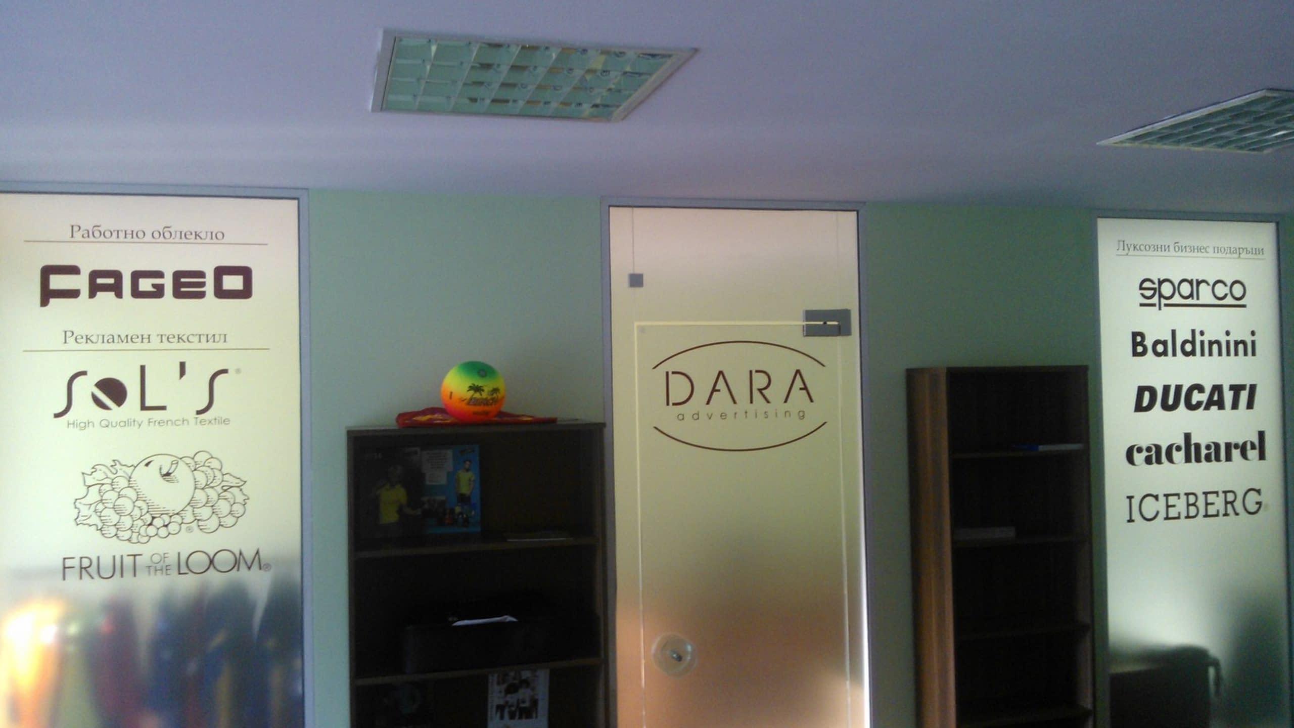 Интериор на офис с матирана врата с лого и светещи пана с лога на партньорски марки.