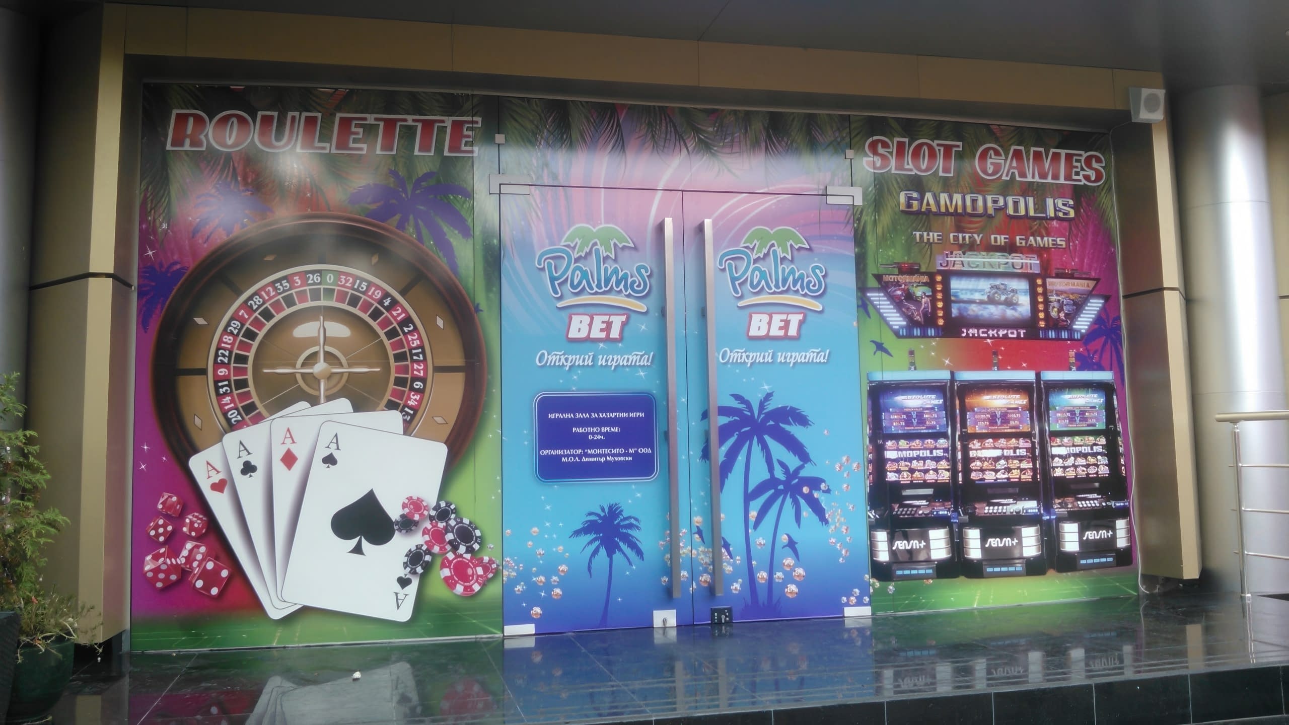 Близък план на облепени с фолио врати и витрини на казино с графики на карти за игра, палми и казино игри.