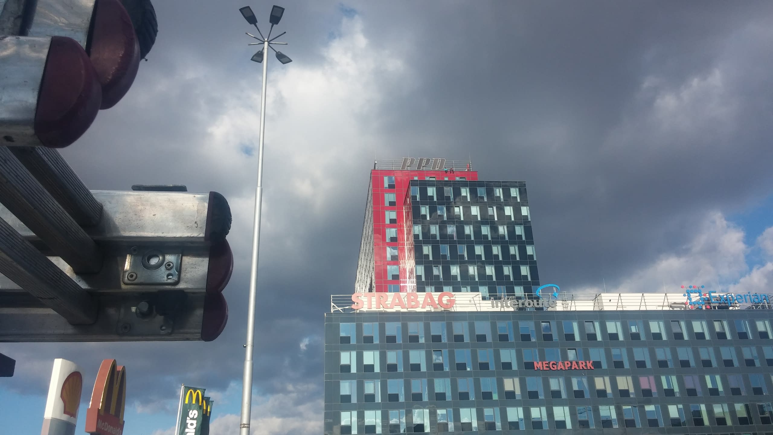 Червена и черна офис сграда с големи букви PPD на покрива, заснети под облачно небе.