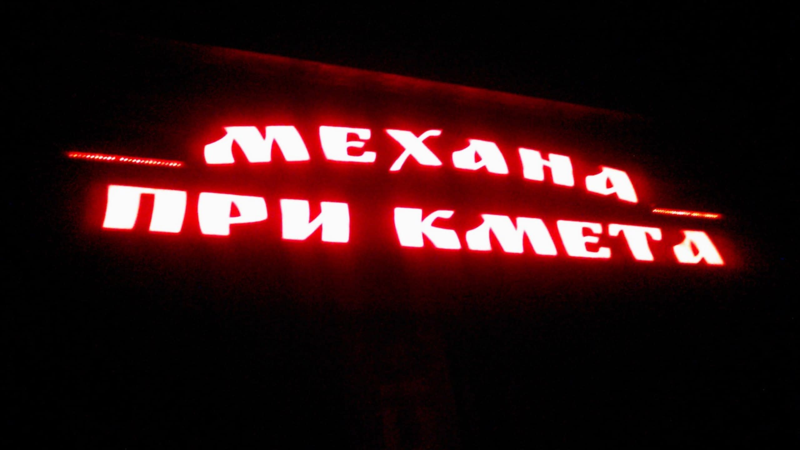 Светещ в червено надпис "Механа При Кмета" на тъмен фон през нощта.