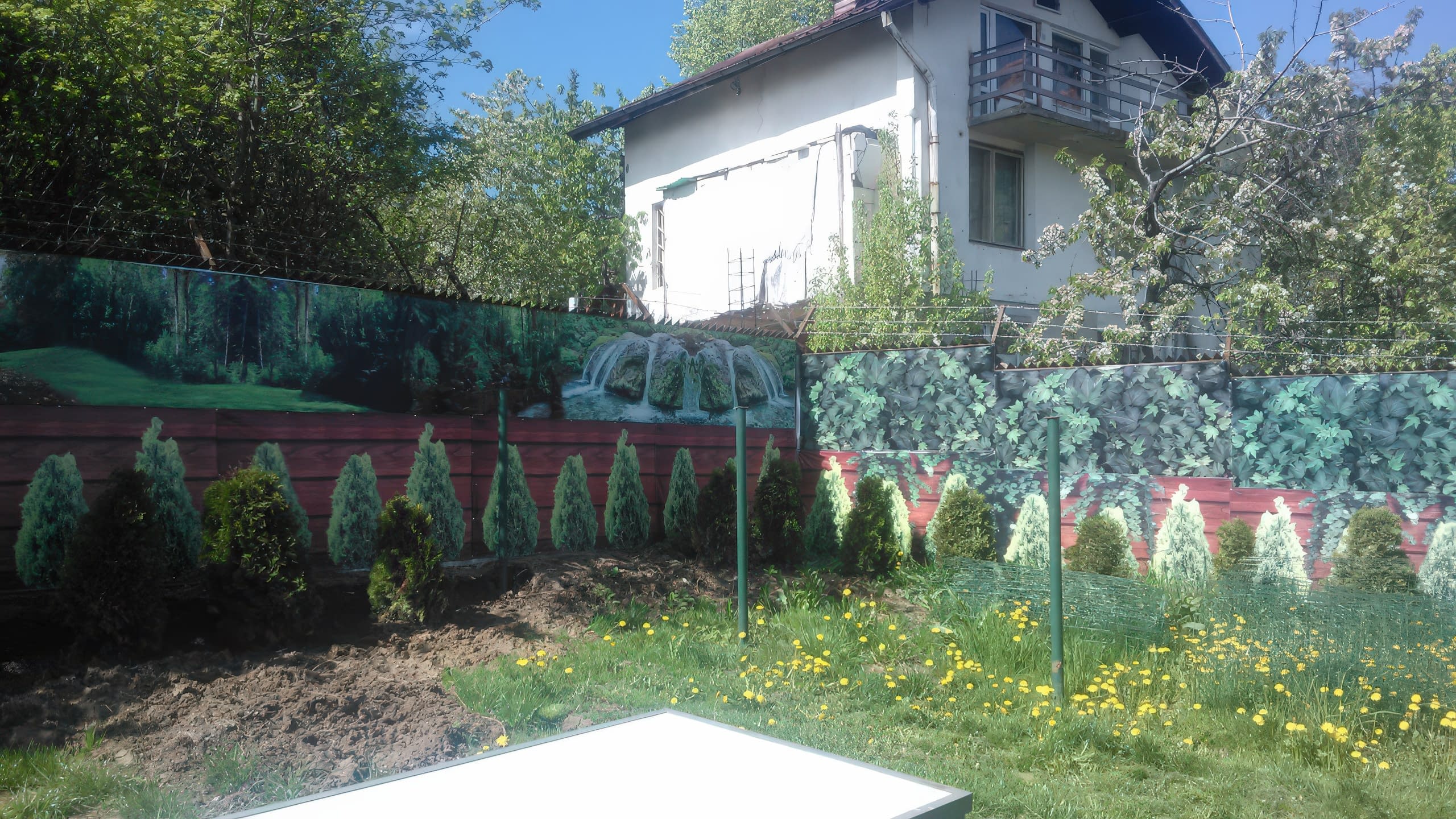 Ограда в градина, декорирана с винилови пана, изобразяващи водопад и зеленина.