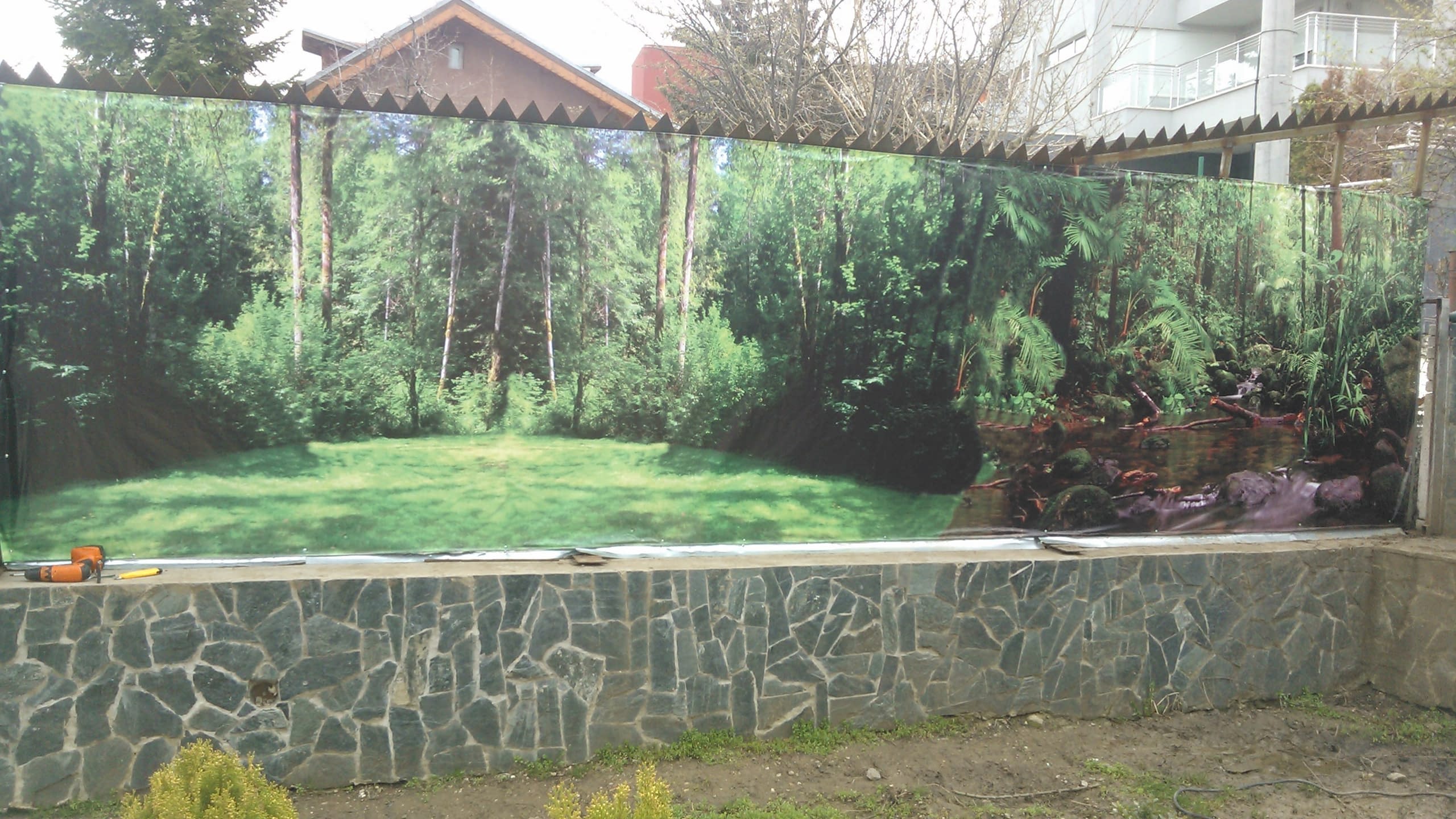 Голям транспарант със снимка на горска поляна, опънат върху ограда в заден двор.