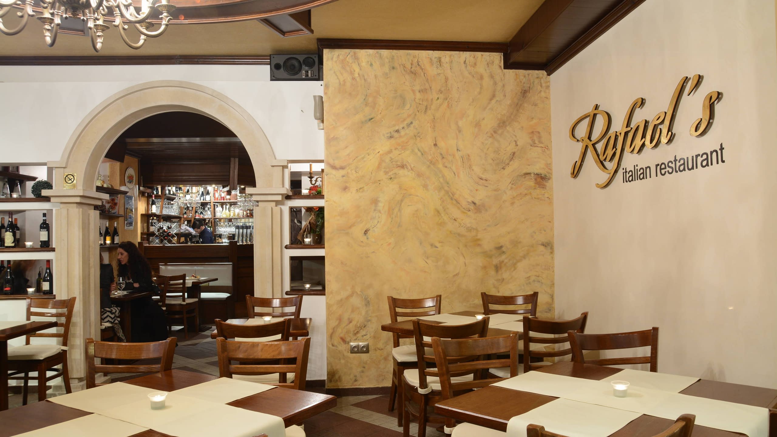 Златист надпис "Rafael's" на стена в интериора на заведение, погледнат под ъгъл.