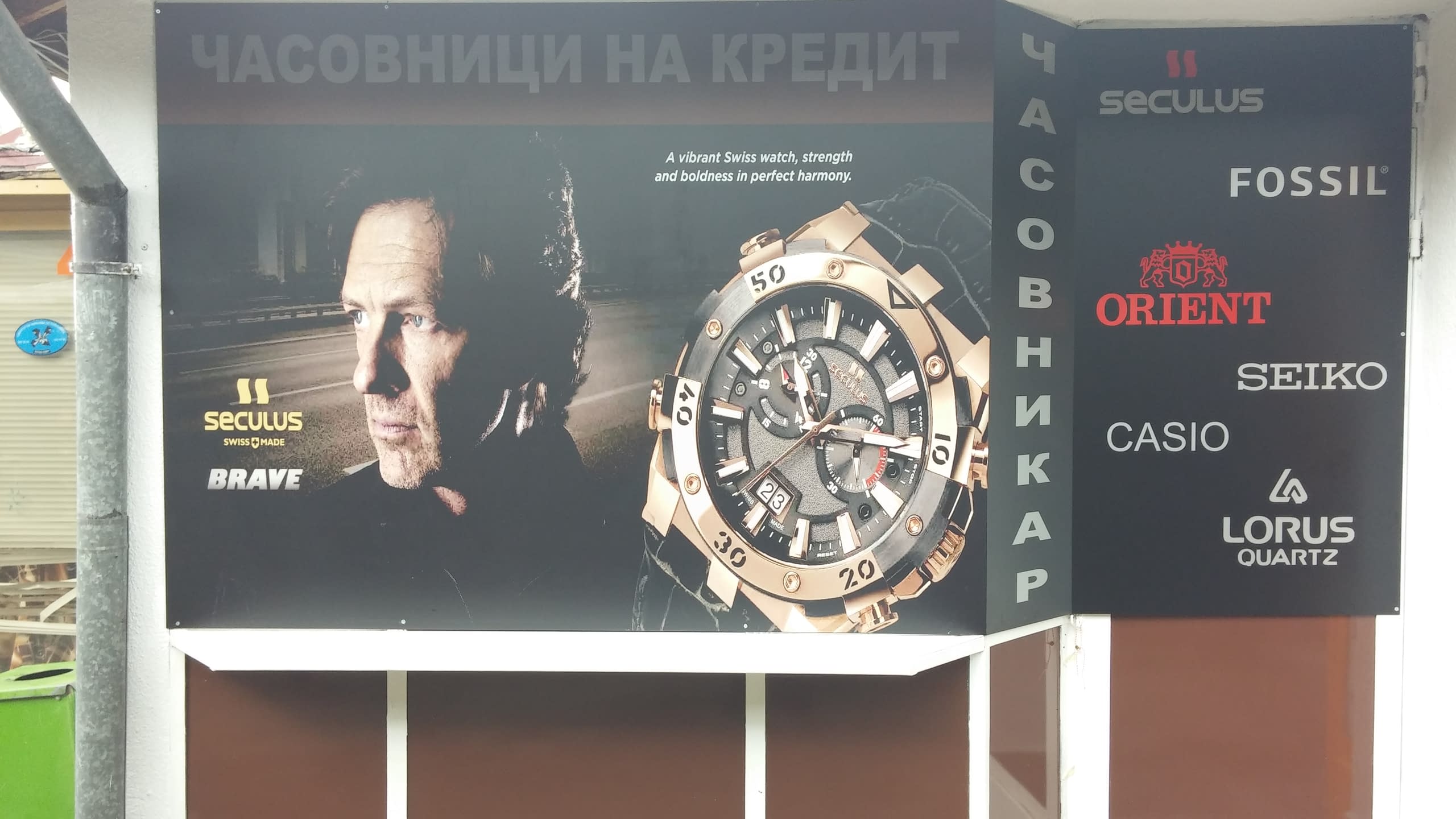 Рекламна табела на магазин за часовници, показваща часовник Seculus и лога на марки като Fossil и Seiko.