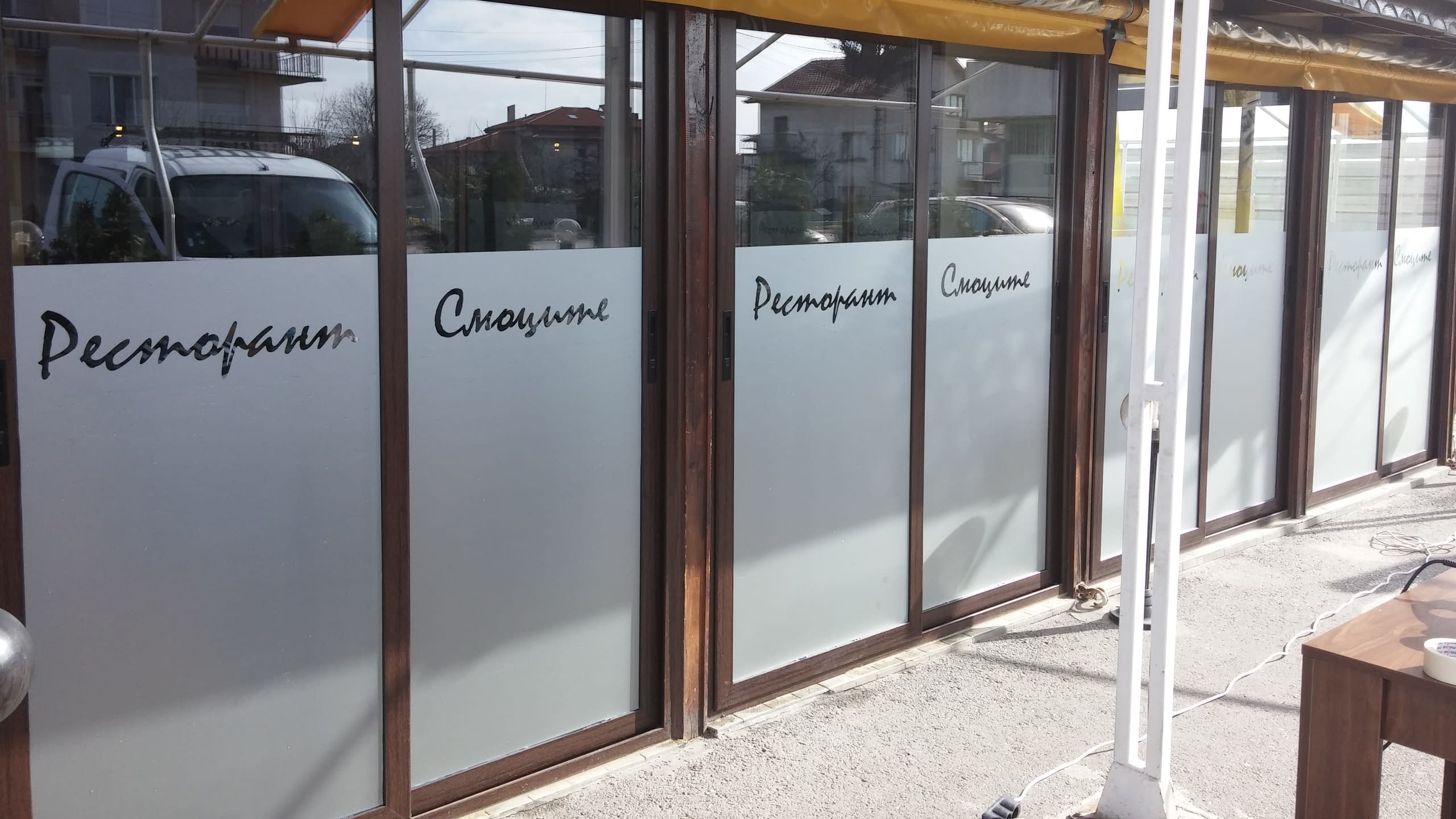 Близък план на стъклени панели с матирано фолио, от което е изрязан надписът "Ресторант Смоците".