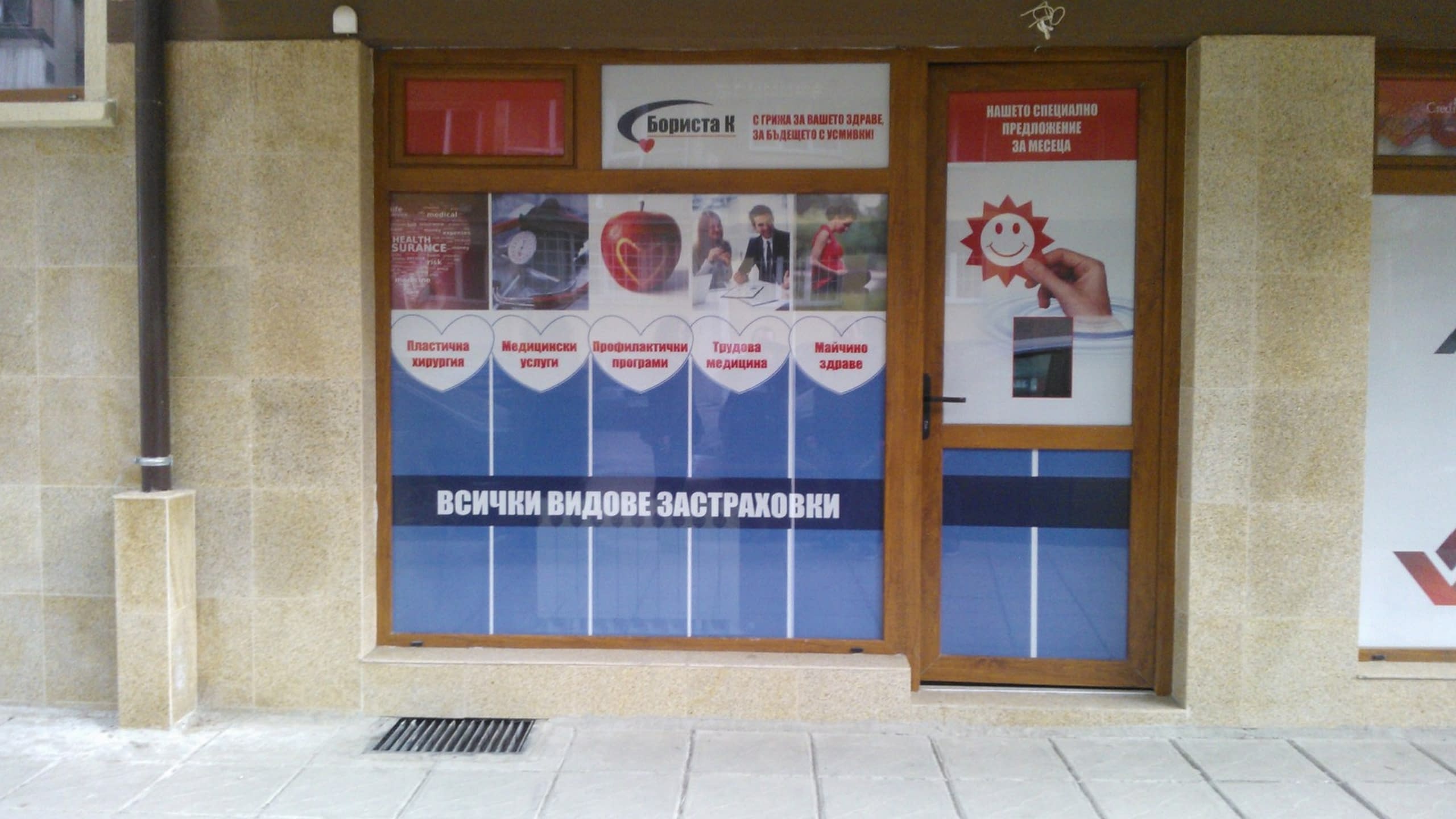 Витрина на застрахователен офис, облепена с перфо фолио с надписи и изображения, описващи различни видове застраховки.