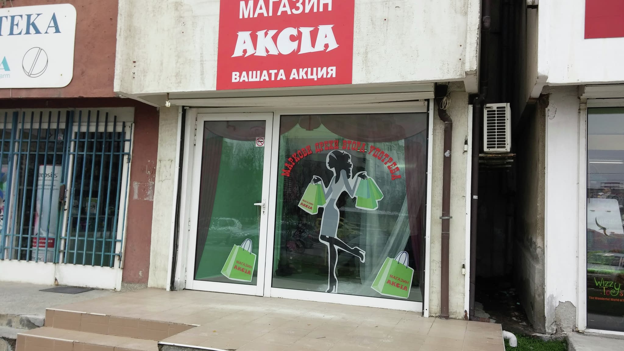 Фронт на магазин ‘Акция’ с червен надпис и витрина с фолио – силует на момиче с пазарски чанти и лозунг за промоции.