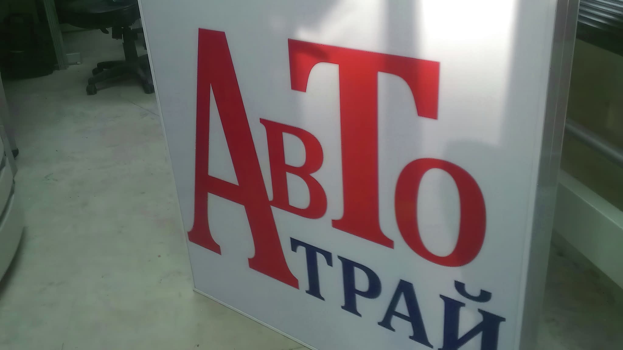 Рекламна табела с надпис 'Авто Трай' – червени и сини букви върху бял фон, създадена за автосервиз или автомобилен бизнес.