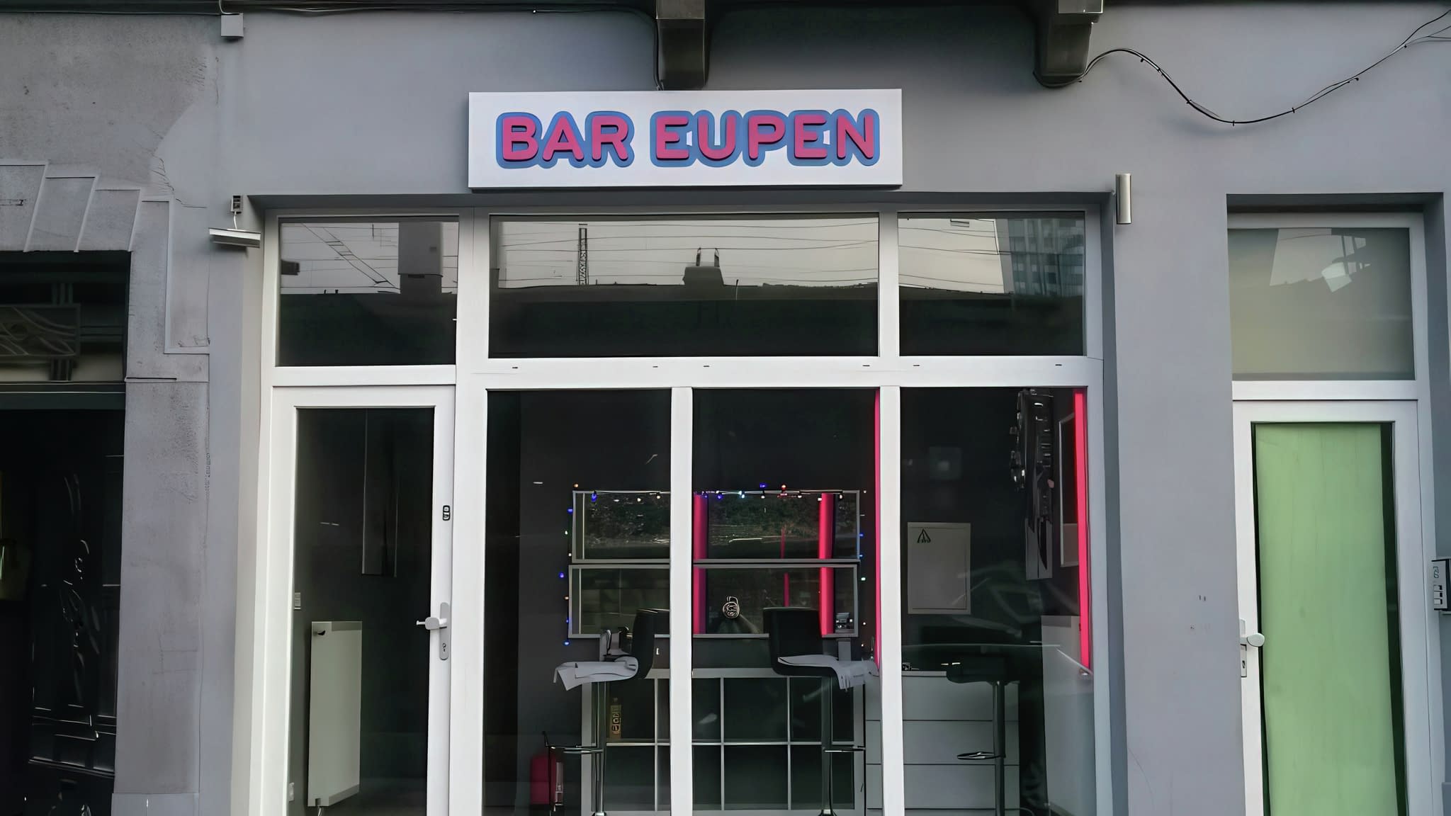 Фасада на „Bar Eupen“ със светеща табела с обемни букви и големи стъклени витрини, илюстриращи ефекта на неоновото осветление.