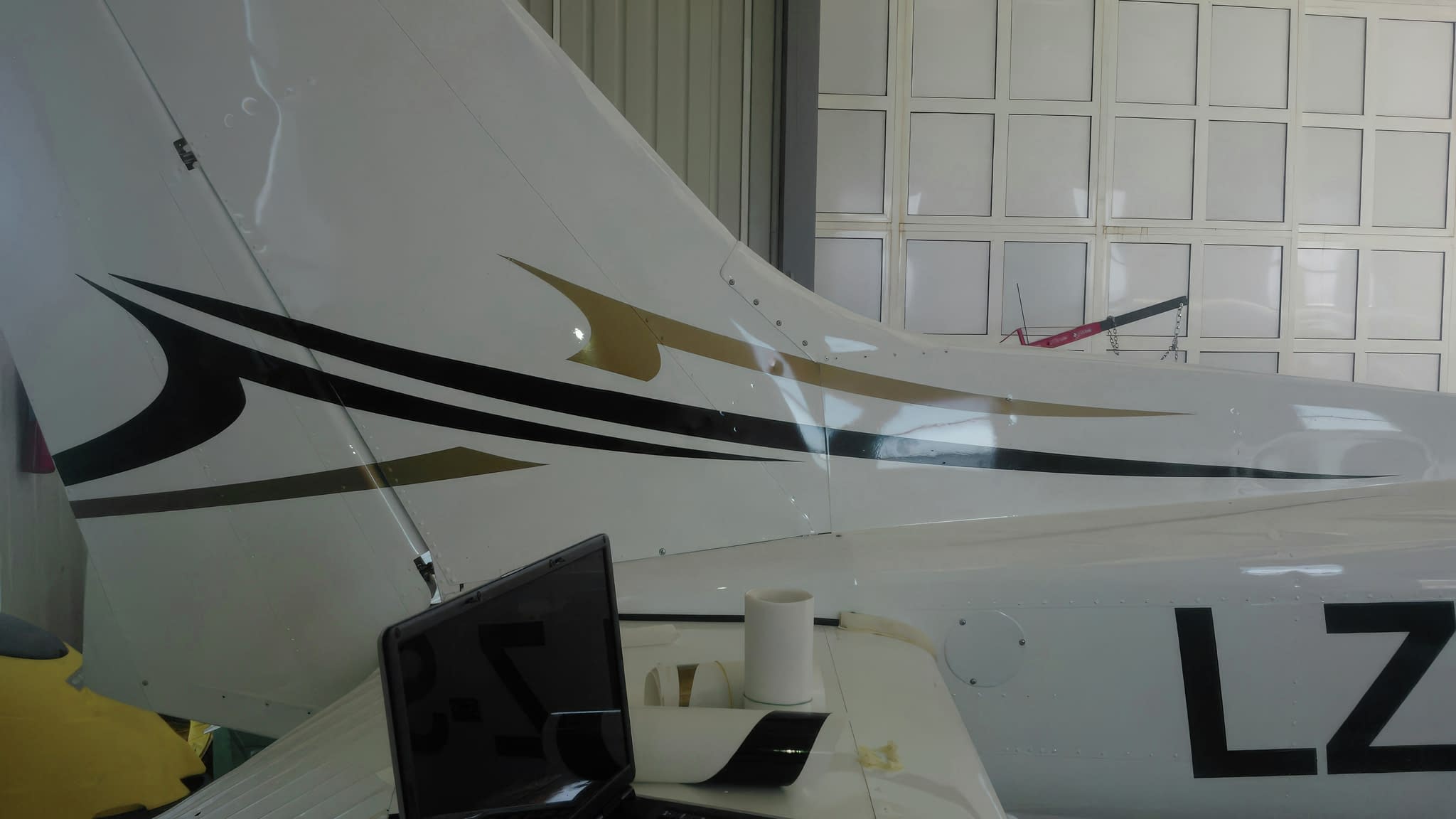 Опашка на малък самолет с черни и златни линии, заснета в хангар.