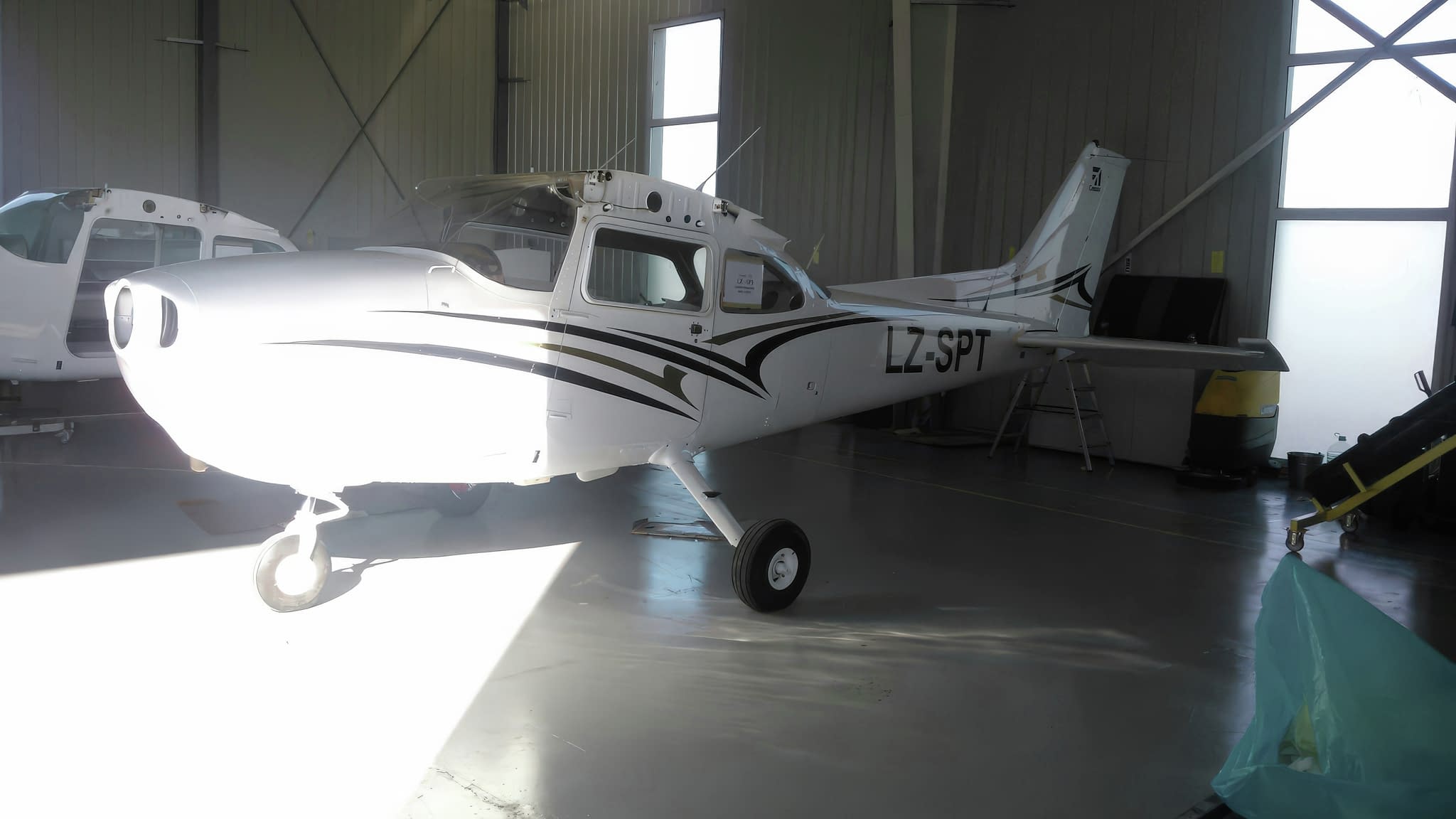 Малък бял самолет с черни декоративни елементи, паркиран в хангар.