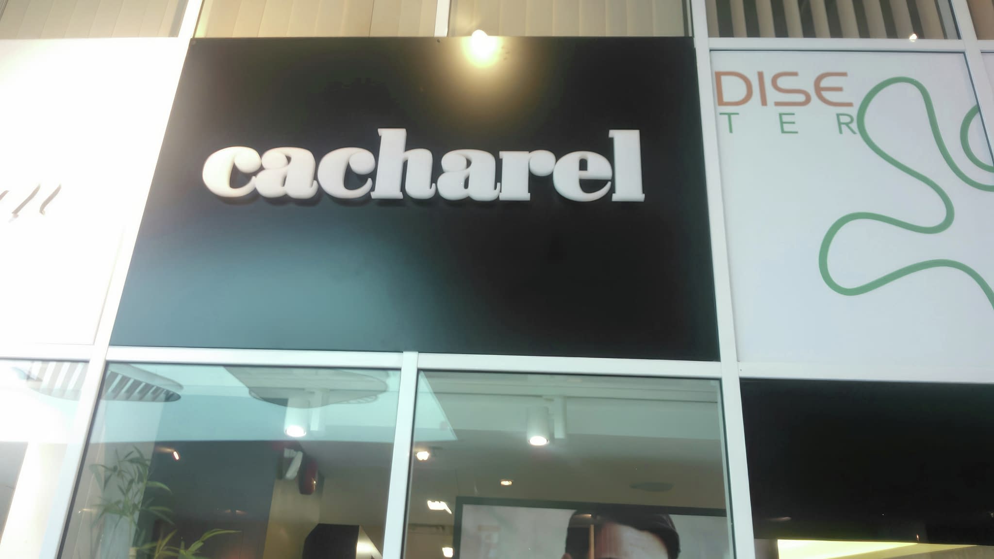 Осветен надпис Cacharel на черен фон, част от елегантна фасада на моден магазин в търговски център.