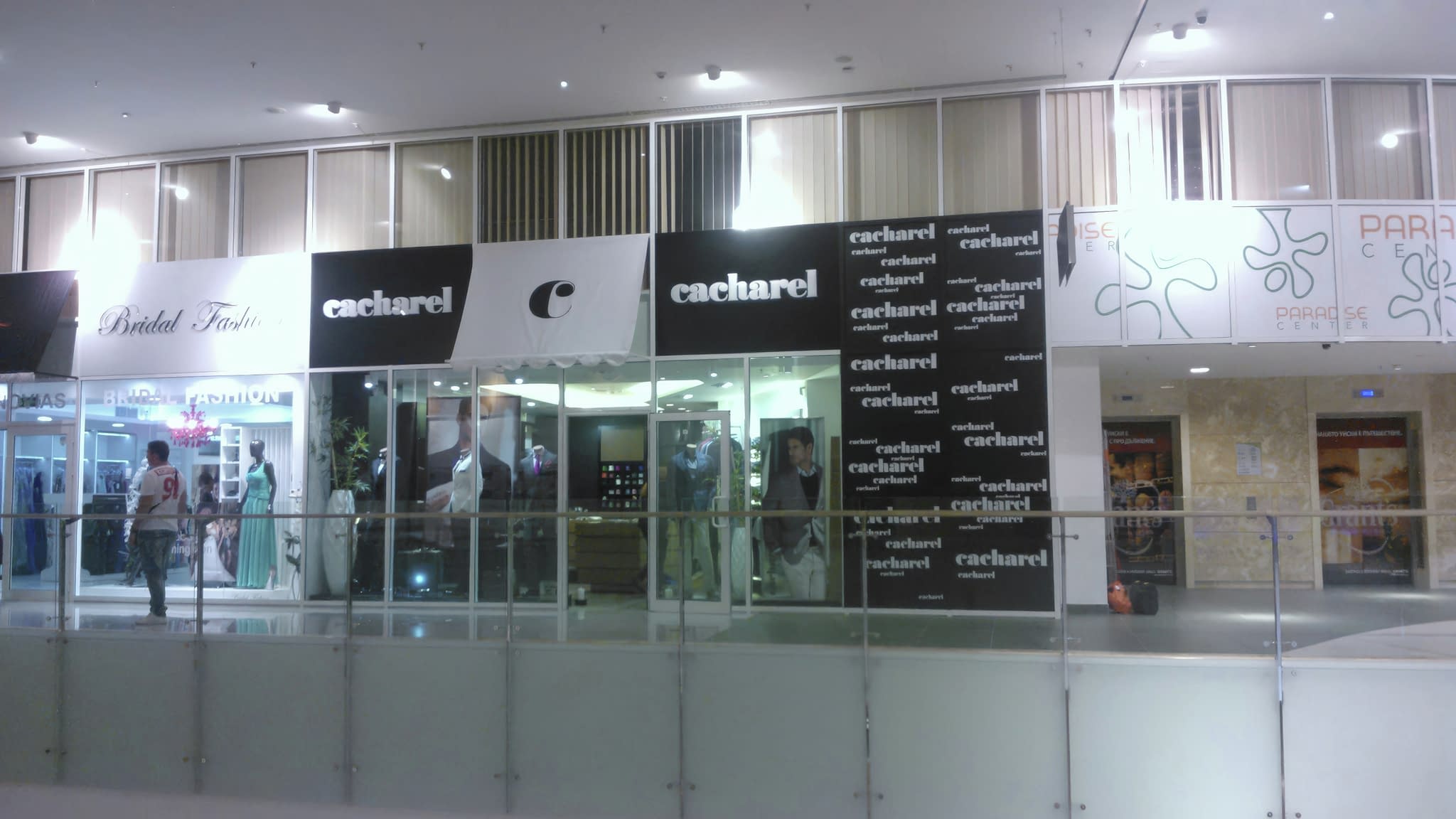Коридор на търговски център с модни витрини, включително Bridal Fashion и Cacharel, с манекени в официални тоалети.