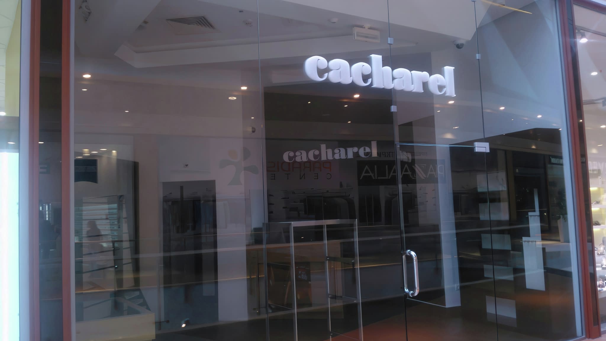 Модерна витрина на магазин Cacharel с обемни букви в бял цвят, изобразени върху стъклена фасада в търговски център.