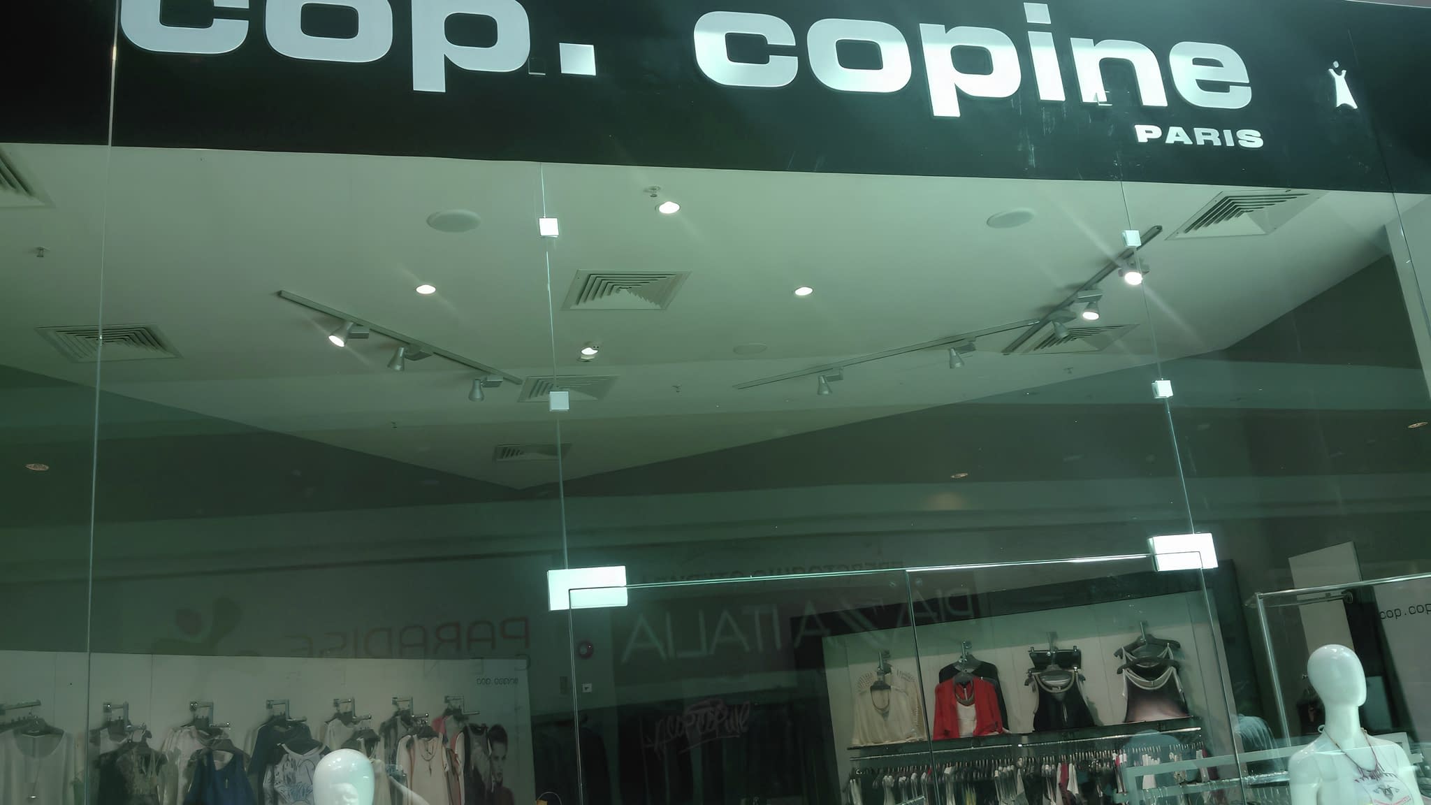 Стъклена витрина на магазин ‘cop. copine Paris’ с черна елегантна табела и изглед към стилни дамски облекла и аксесоари на закачалки.