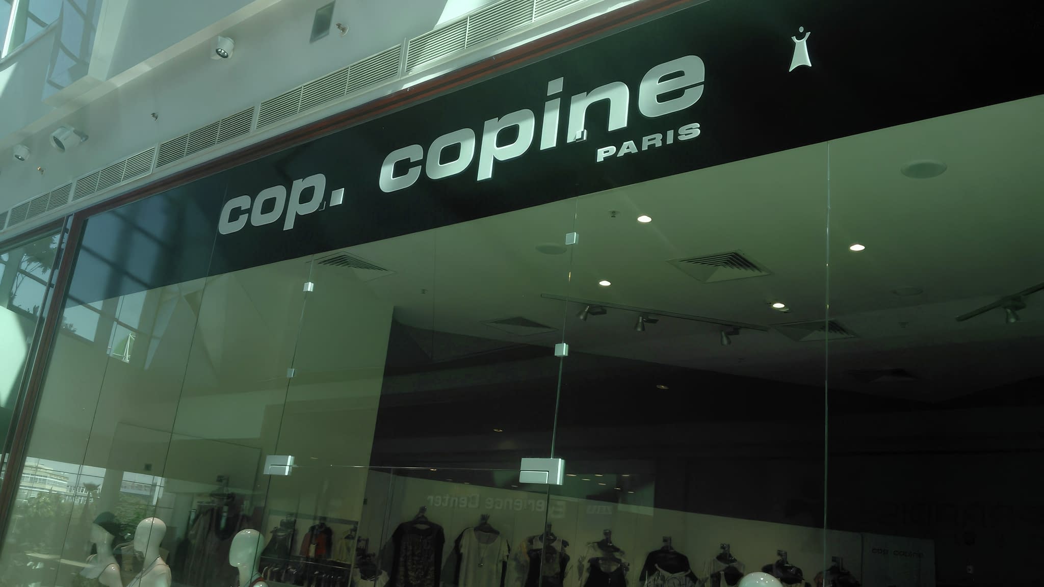Фасада на магазин ‘cop. copine Paris’ в търговски център с елегантна черна рекламна табела и стъклена витрина със стилни облекла.