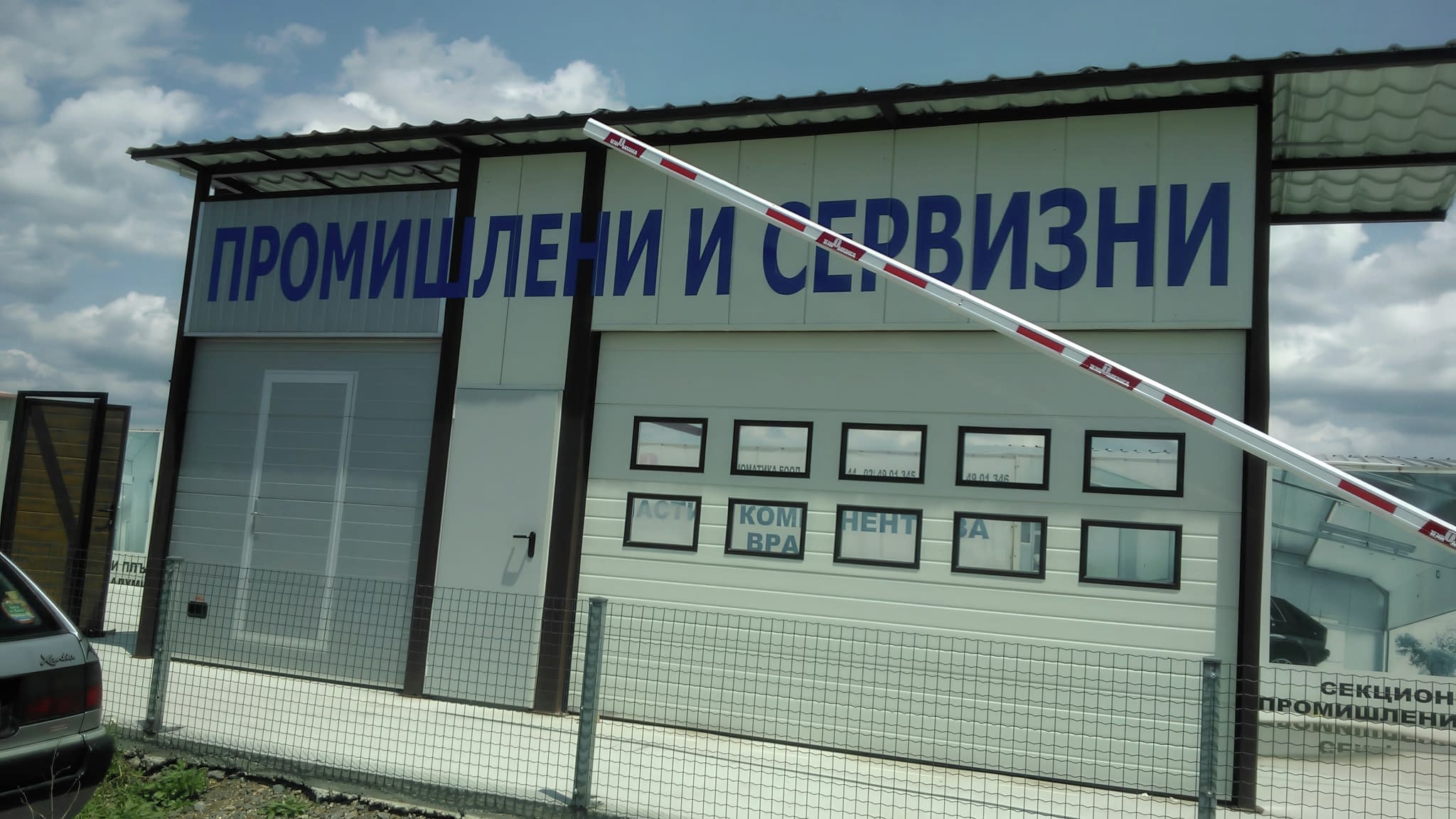 Екстериор на сграда с големи сини надписи „ПРОМИШЛЕНИ И СЕРВИЗНИ“, обозначаващи промишлени секционни врати