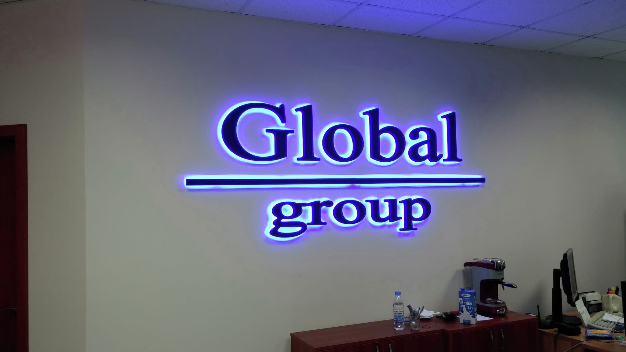 Светеща табела за стена с надпис „Global group“, елегантен шрифт с лилаво сияние, подходяща за корпоративни офиси.