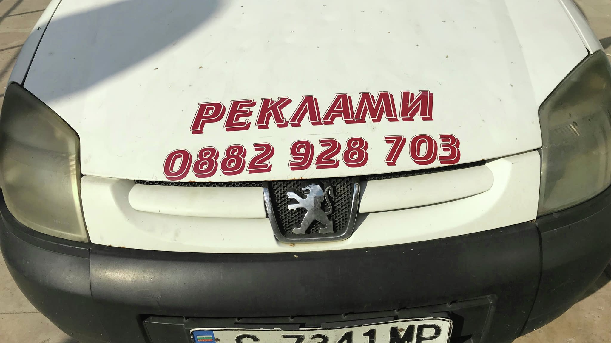Реклами за коли – преден капак на бял ван Peugeot с голям надпис „РЕКЛАМИ“ и телефон за контакт, демонстриращ автомобилно брандиране.